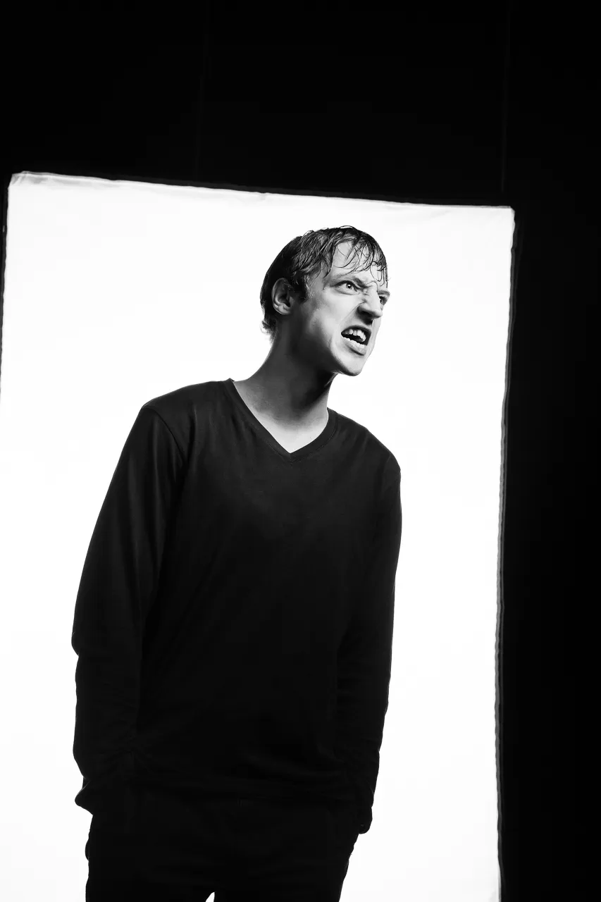 An actor in a V-neck jumper pulls a sneering face.