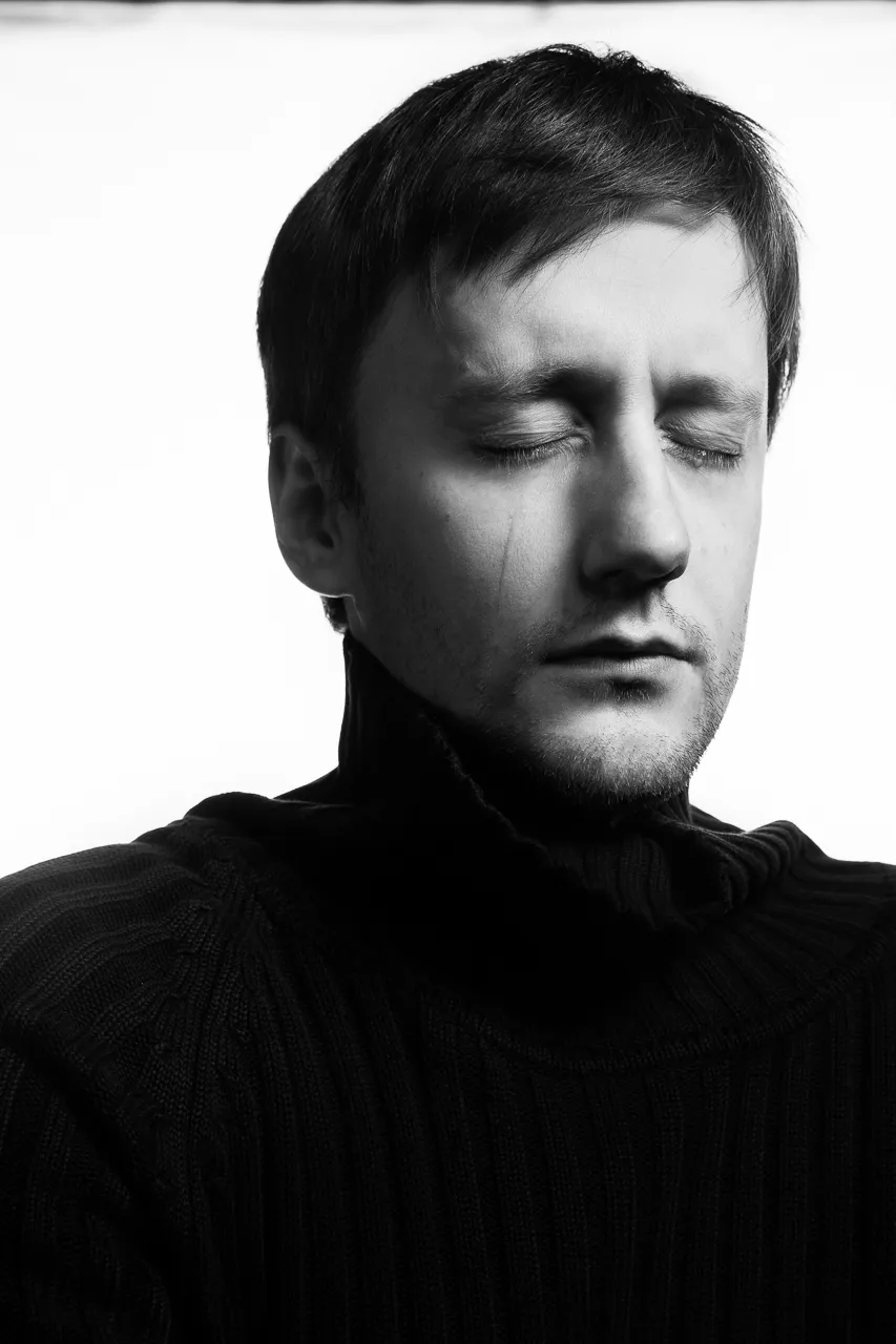 An actor in a black polo neck stands with his eyes closed.