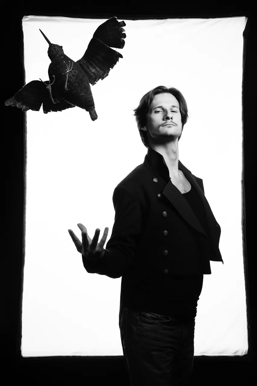 An actor reaches towards a stuffed long-billed bird hanging in the air above him.