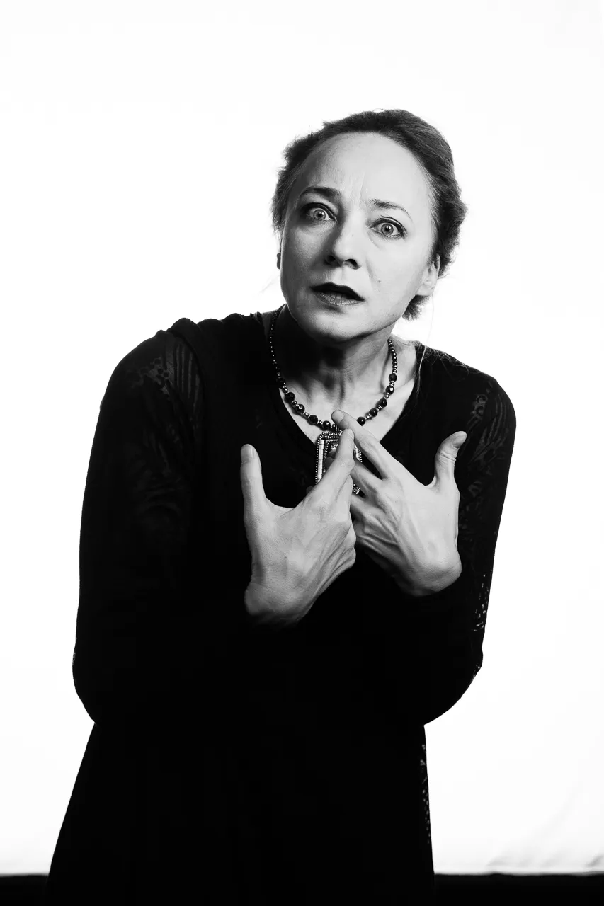 A wide-eyed actress presses her hands to her chest.