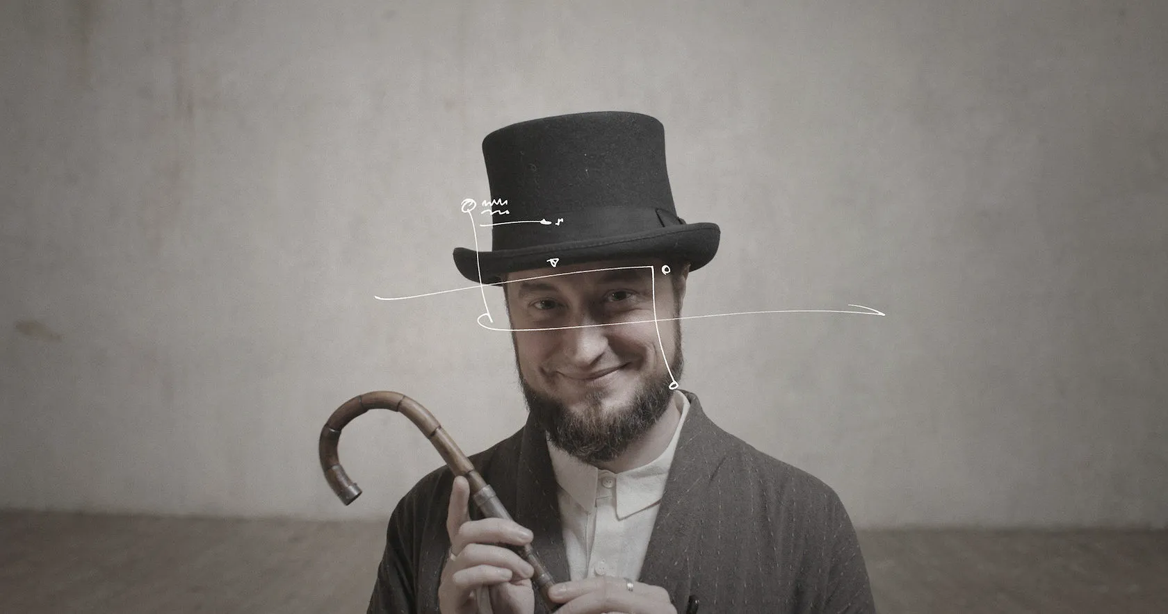 A bearded man in a top hat grins and grips a walking cane.