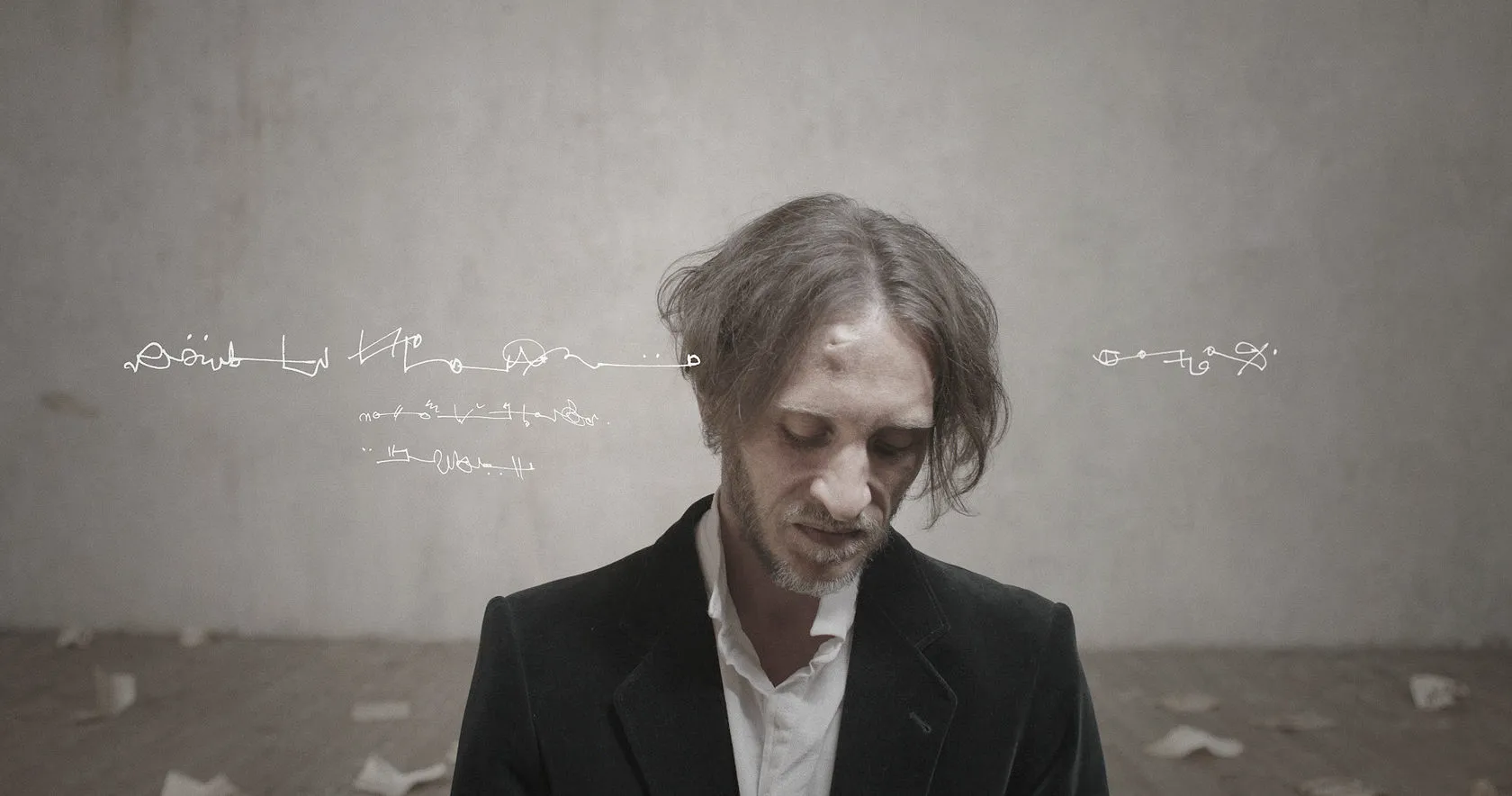 A dishevelled man in a dark coat looks down, a line of scribbled script beside him.