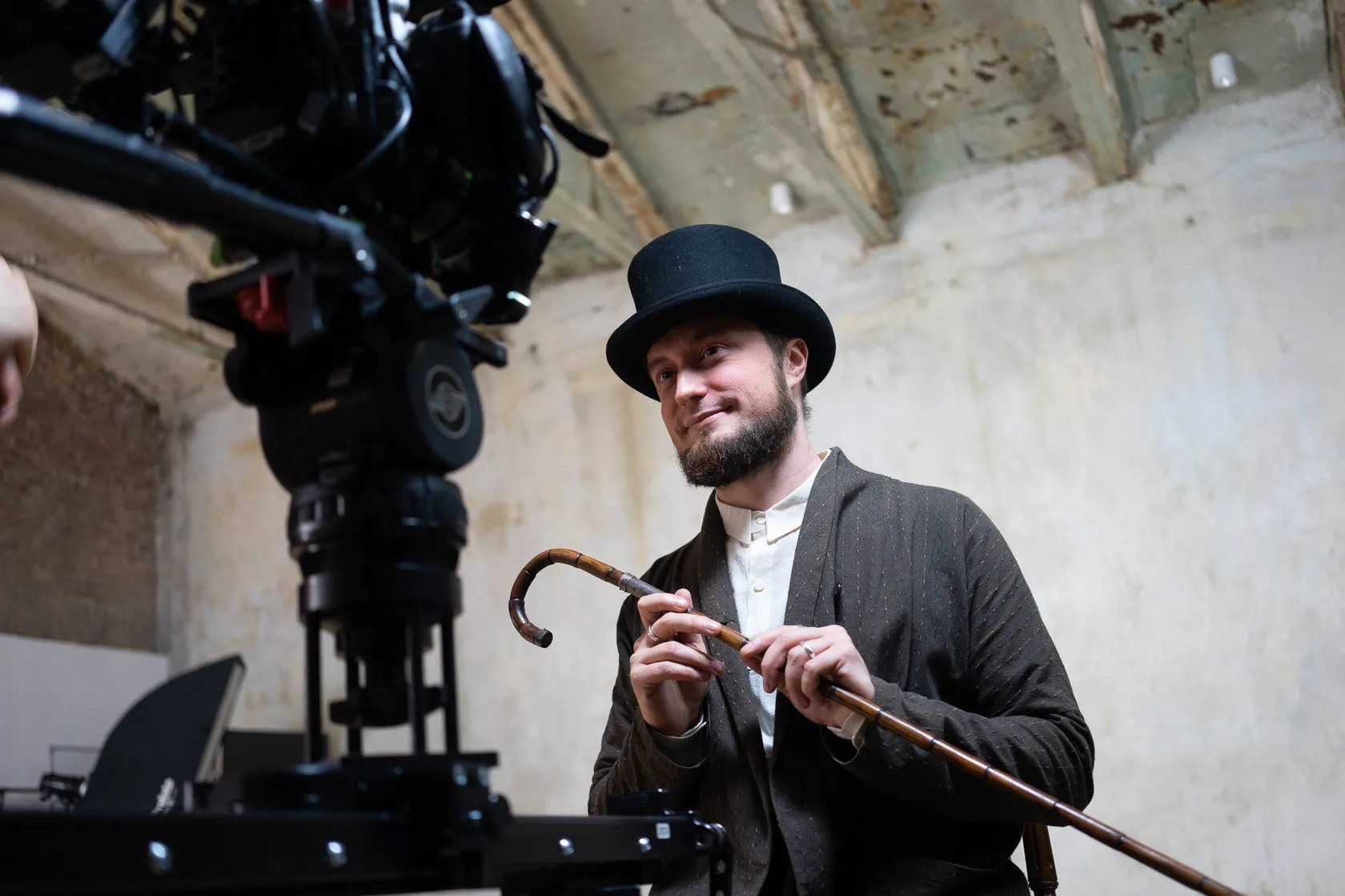 Behind the scenes: the actor in the top hat smiles past the film camera, cane in hand.