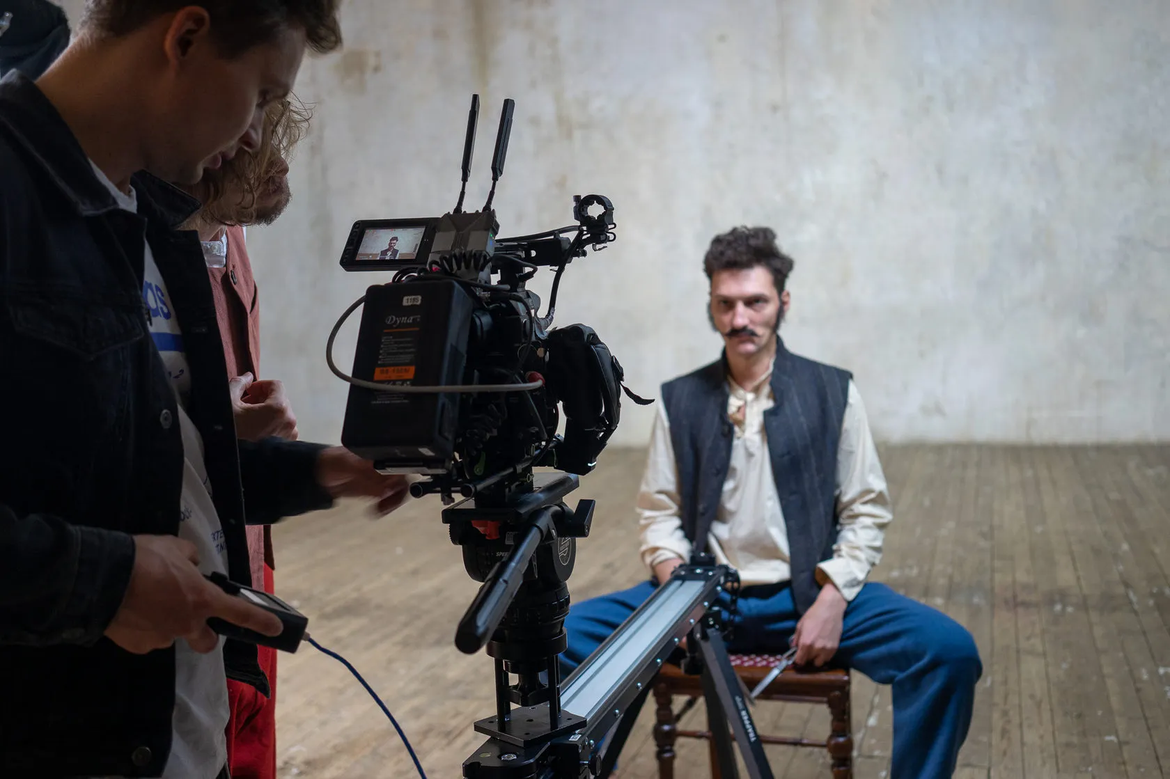 Behind the scenes: the crew checks the camera while an actor in a waistcoat sits waiting.