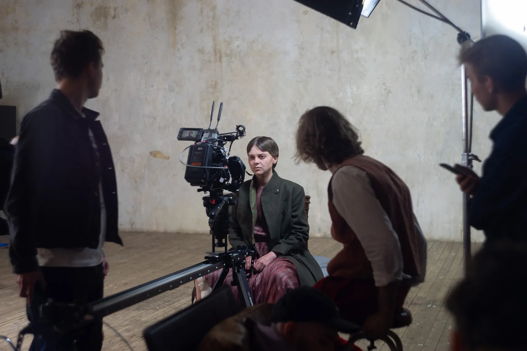 Behind the scenes: an actress sits by the camera on its slider, the crew around her.
