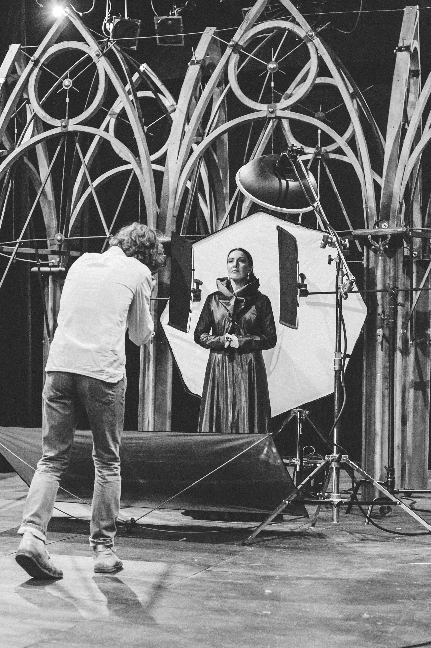 Behind the scenes: an actress in a long dark coat poses in front of the light on stage.