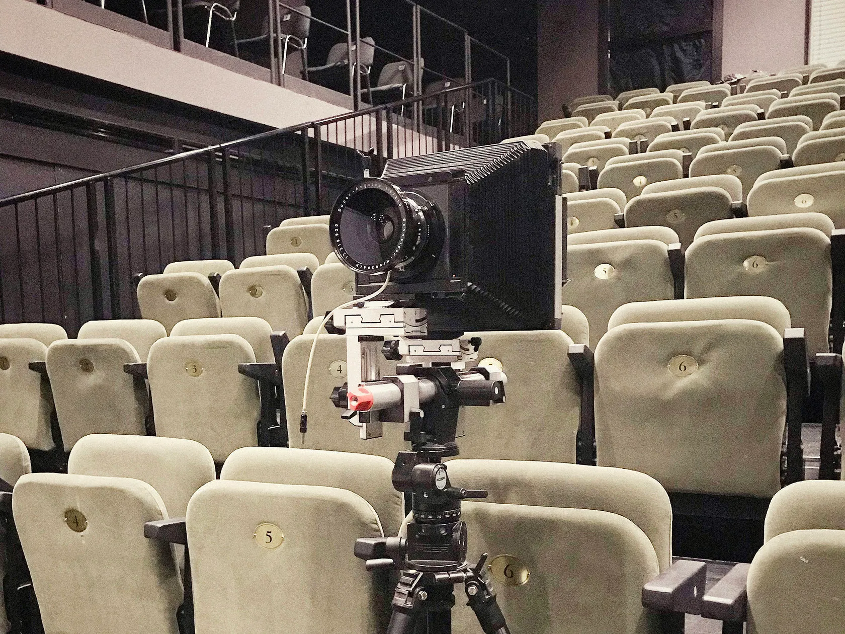 A large-format camera on a tripod stands among the theatre’s seats.
