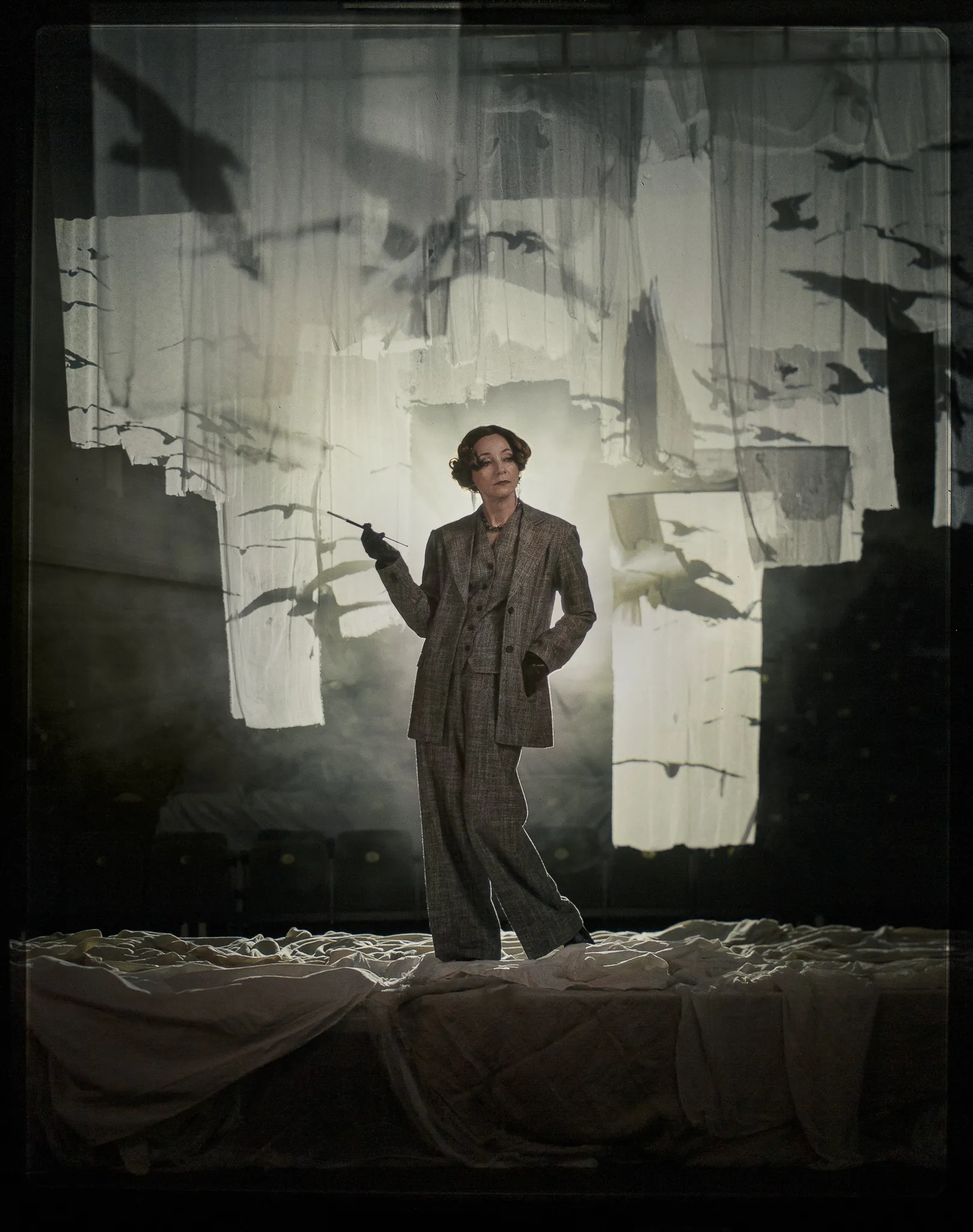 Galina Tyunina as Arkadina, in a tweed trouser suit, holds a long cigarette holder before strips of gauze.