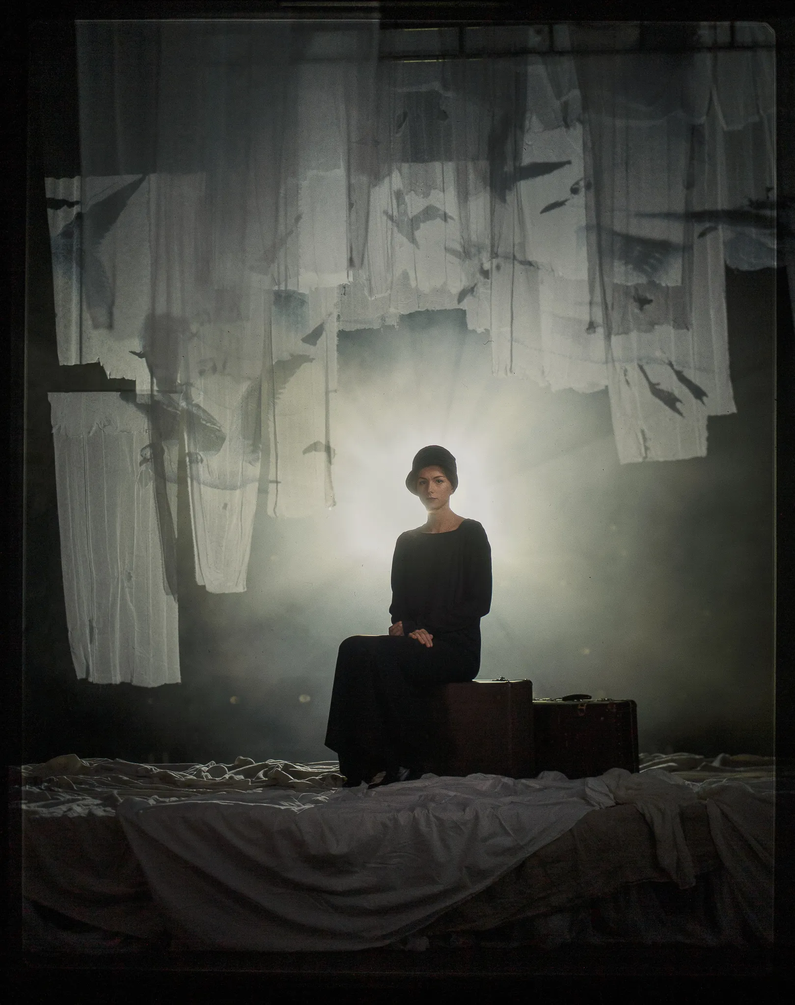 Serafima Ogaryova as Masha sits on a suitcase in a long black dress.