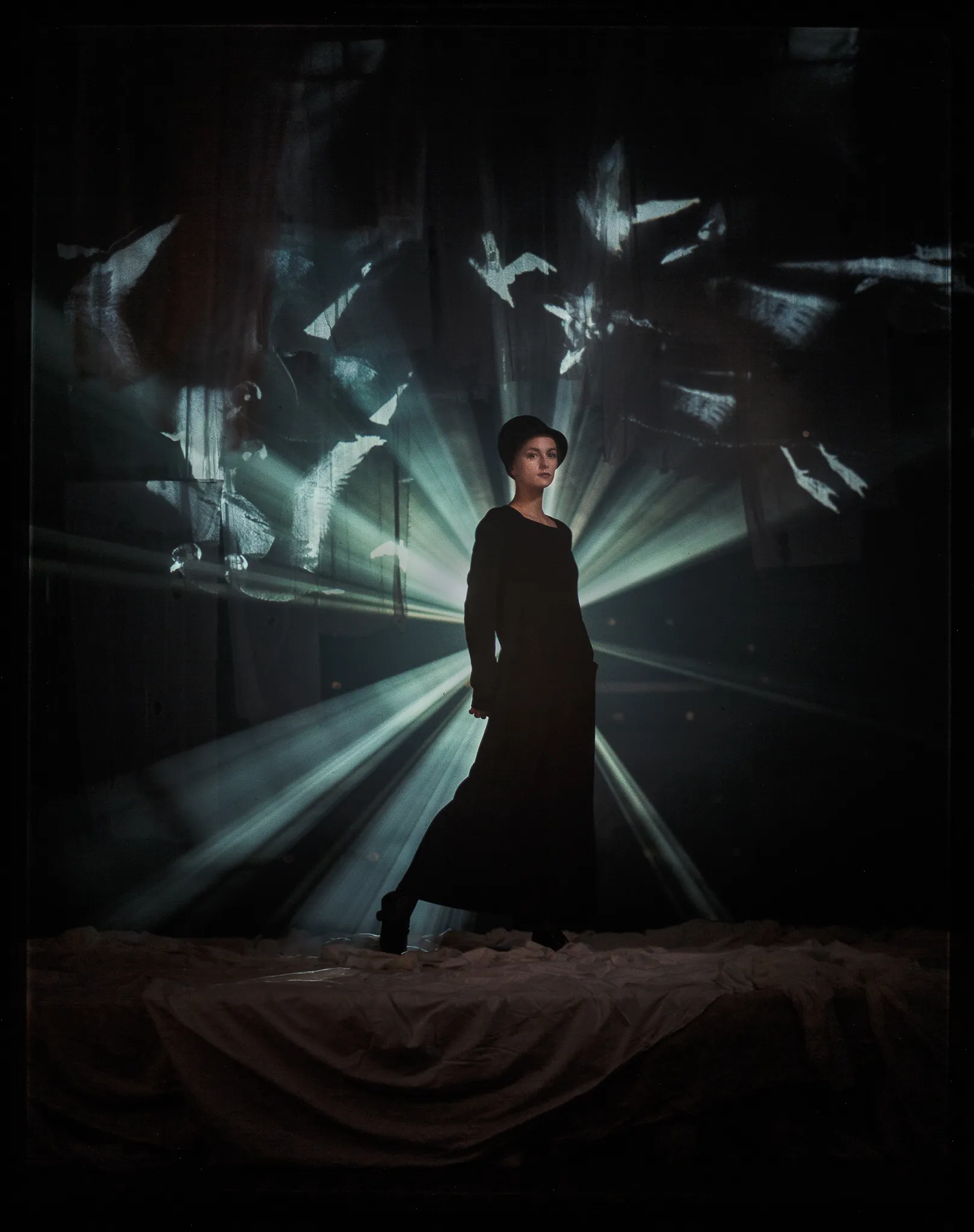 Serafima Ogaryova as Masha walks through rays of light and projected gulls in a black dress.