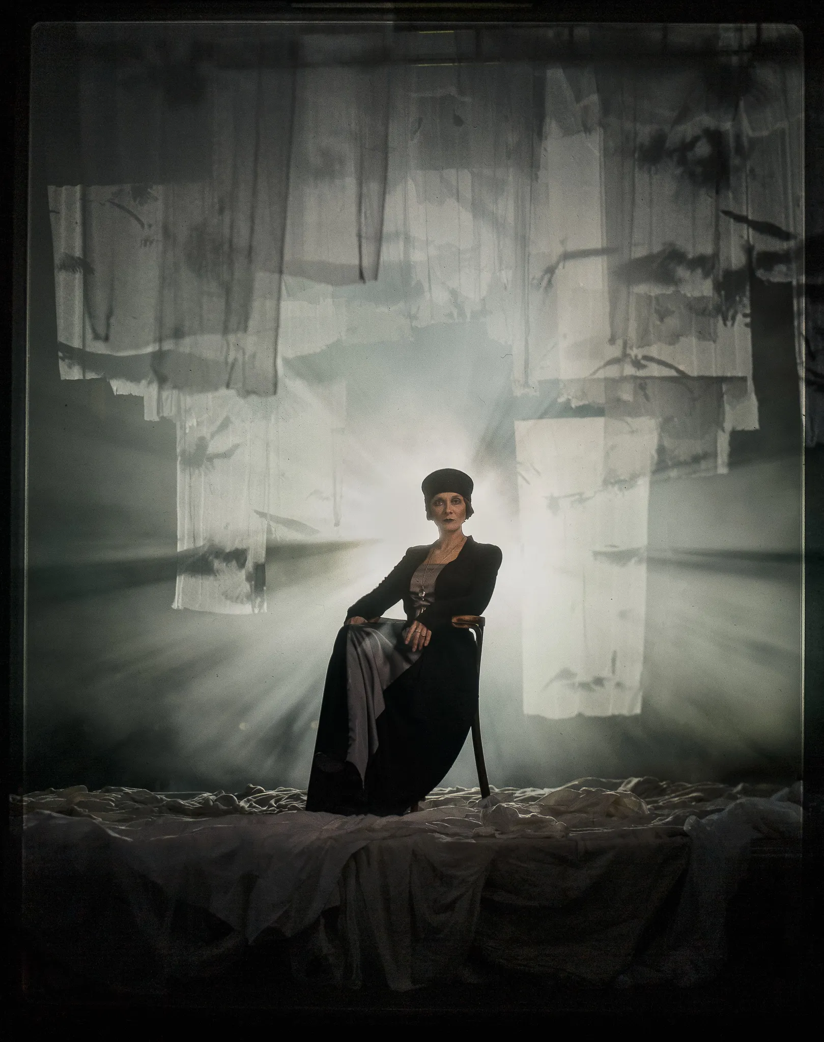 Natalia Kurdyubova as Polina sits on a bentwood chair, lit from behind through strips of gauze.
