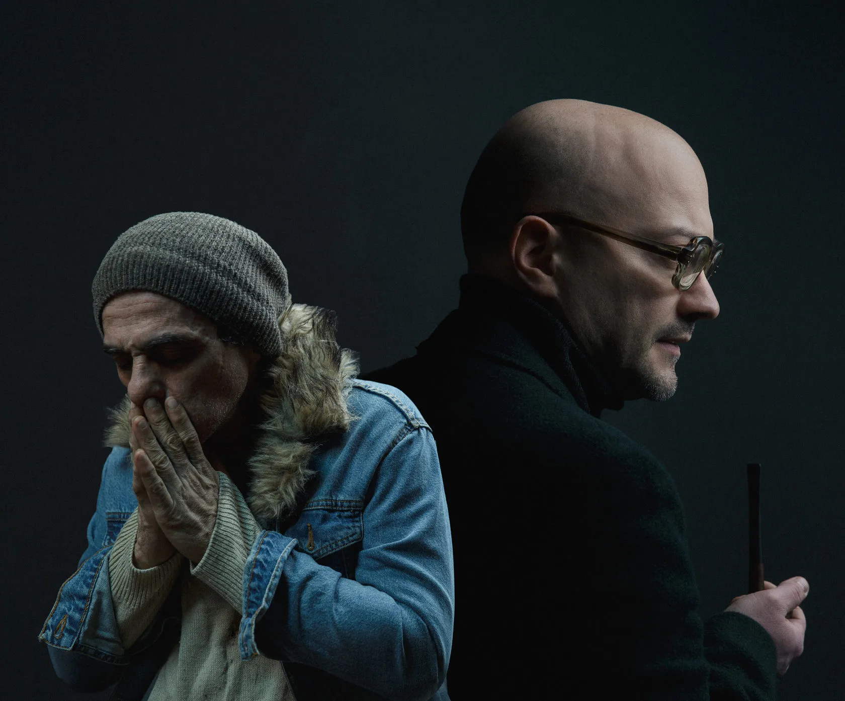 The two characters: a man in a knit cap and denim jacket, hands to his mouth, and a bald man in glasses.