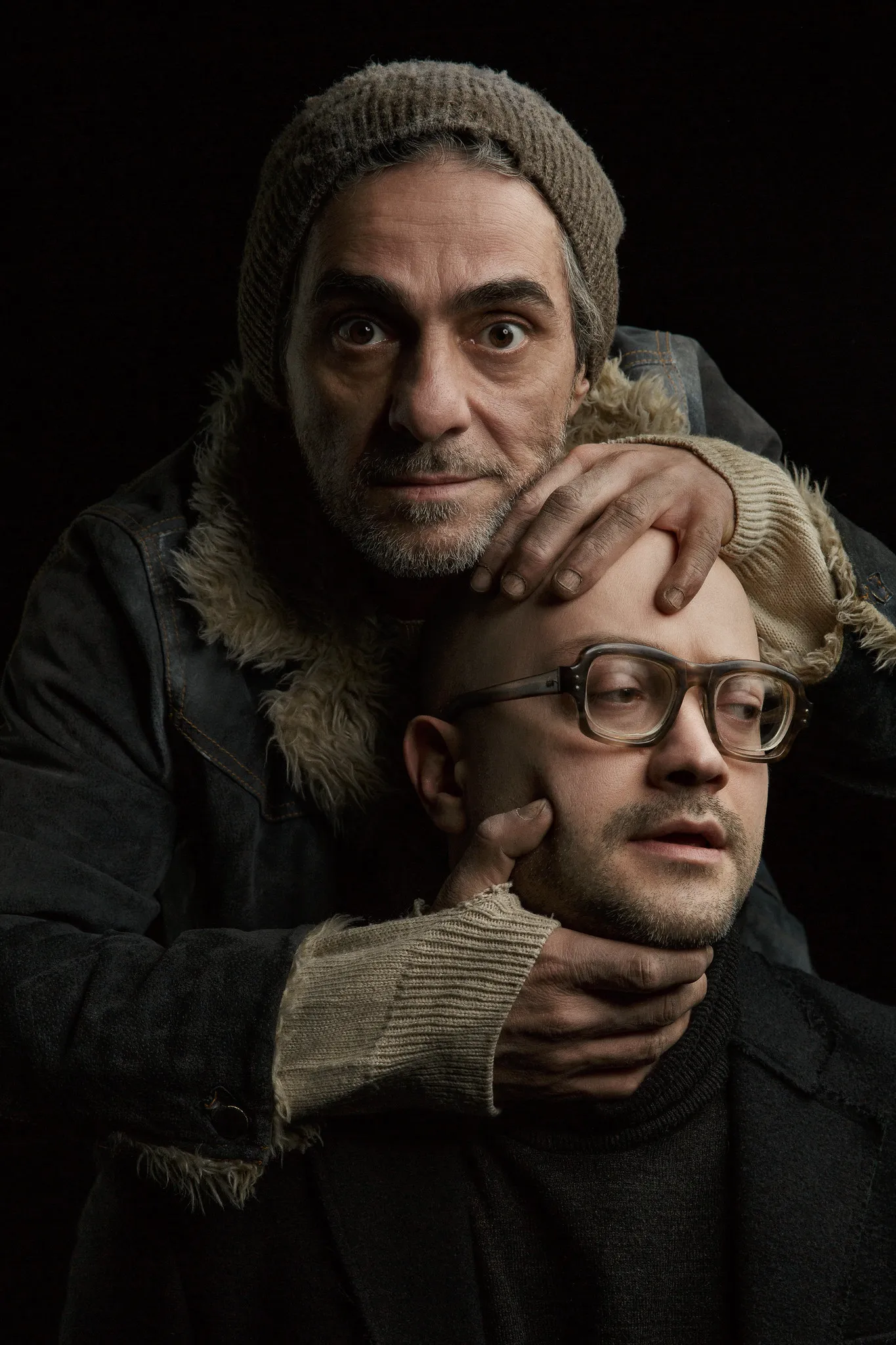 Key visual: the homeless man in a knit cap grips the head of the bald man in glasses.