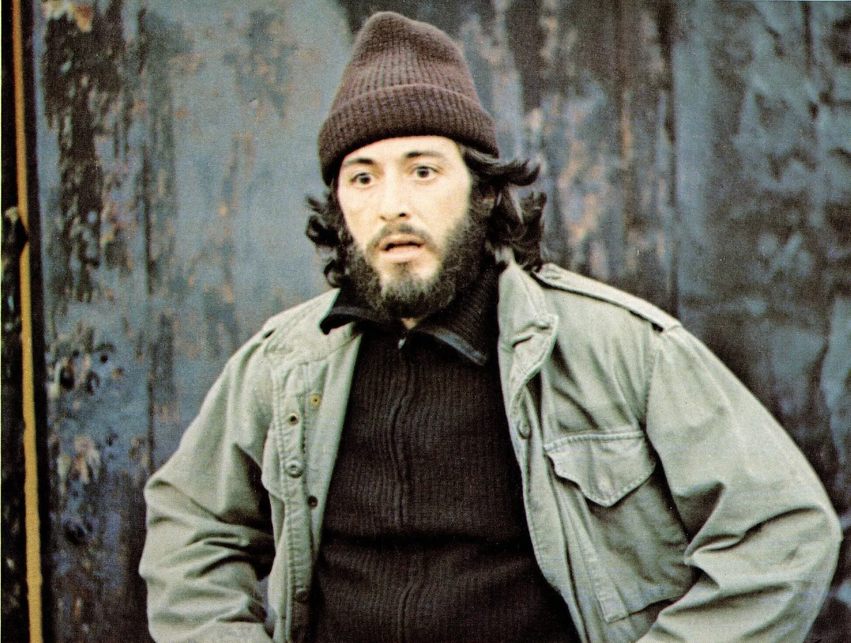 Reference: a bearded man in a knit cap and army jacket against a peeling wall.