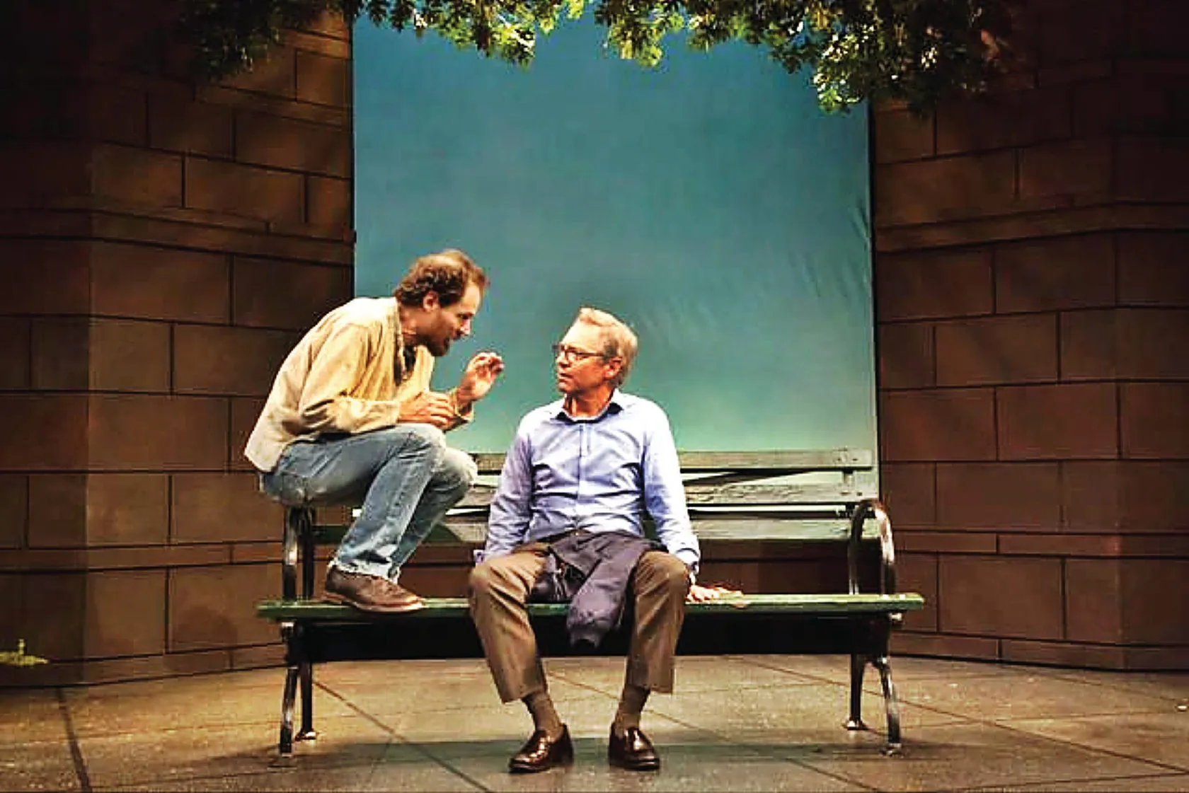 Reference: two men talk on a park bench in a stage set.
