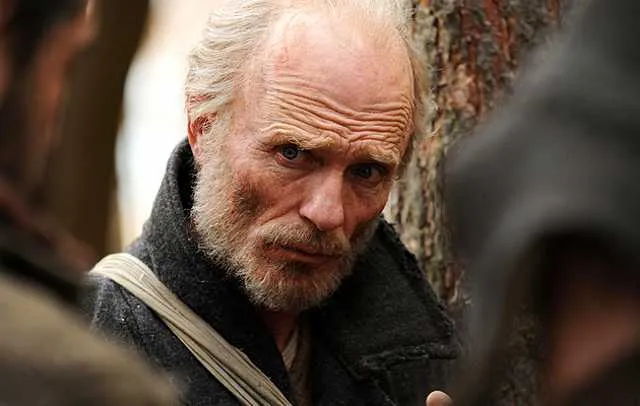 Reference: a weathered, grey-bearded man in a heavy coat with a shoulder strap.