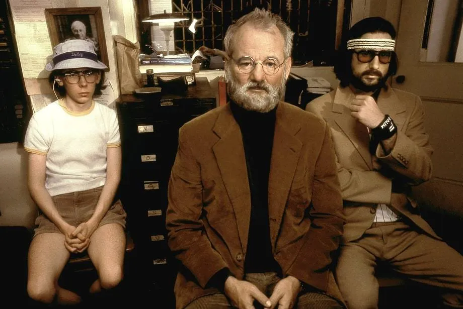 Reference: a film still of a boy and two men sitting in a cluttered room.