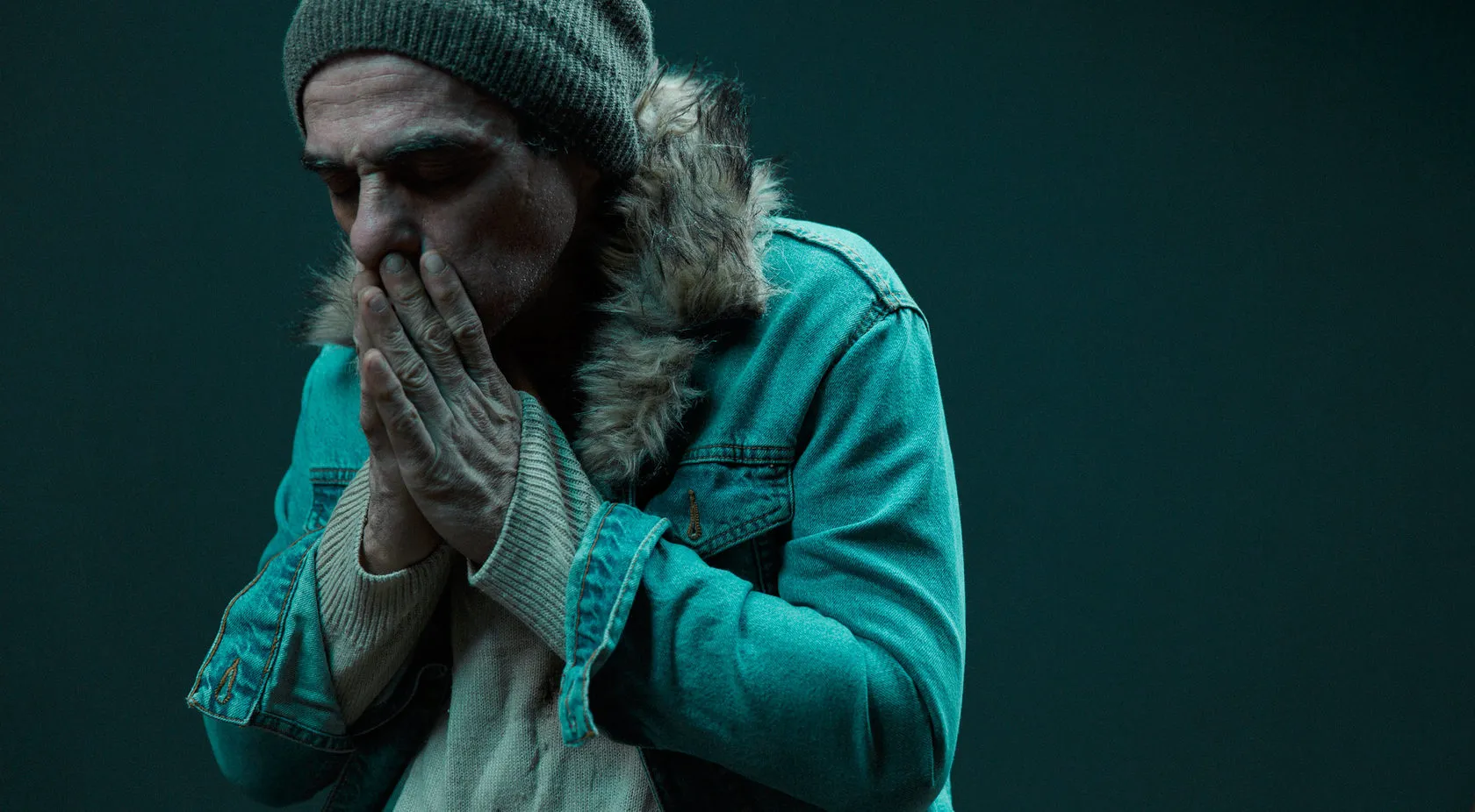 The man in the denim jacket covers his mouth with both hands.