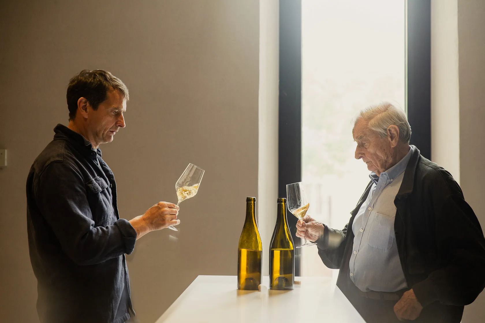 Jean-Louis Chave and his father taste white wine by a window, two bottles between them.