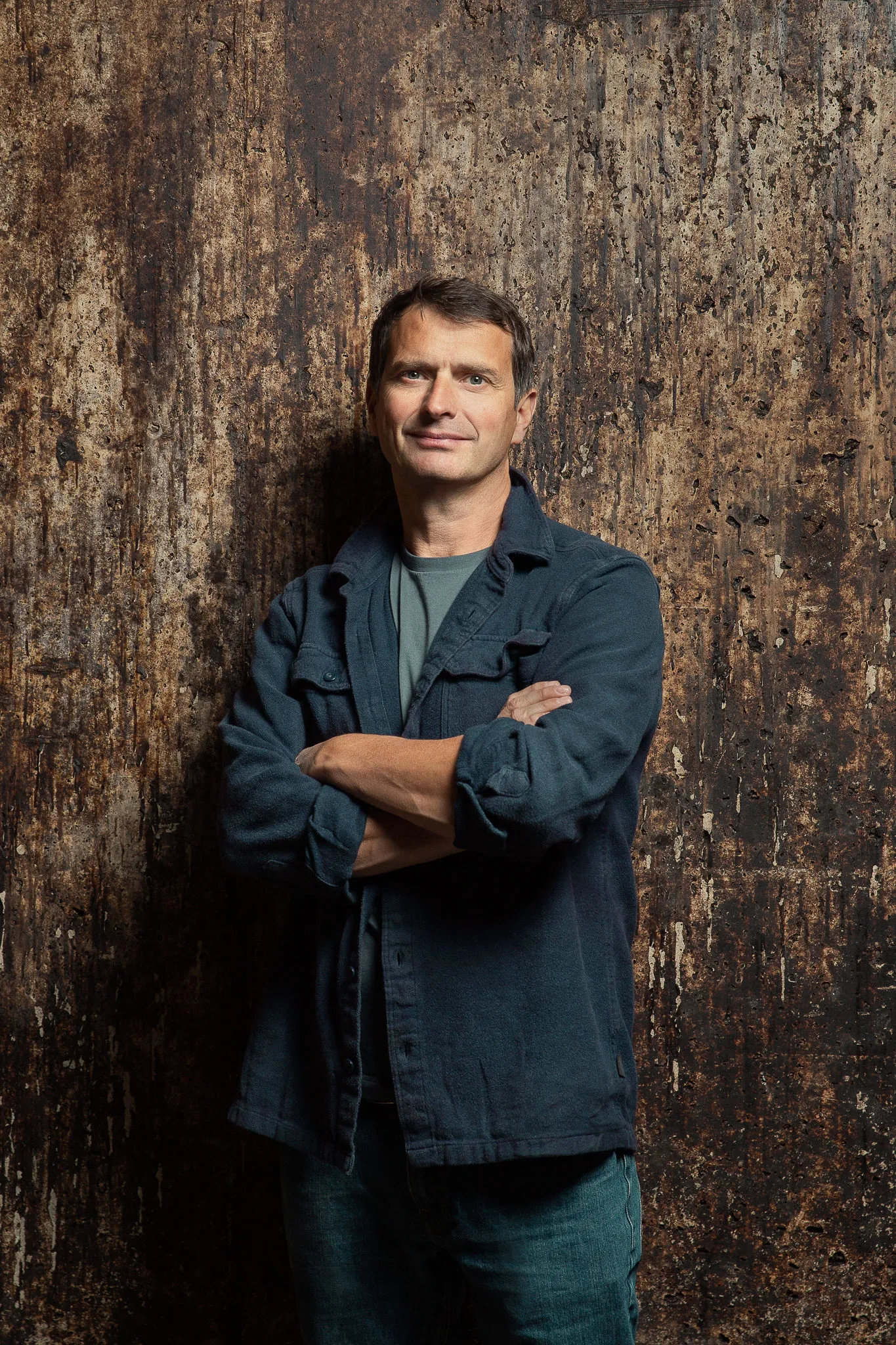 Jean-Louis Chave, arms crossed, leans on the mottled wall of the old cellar.