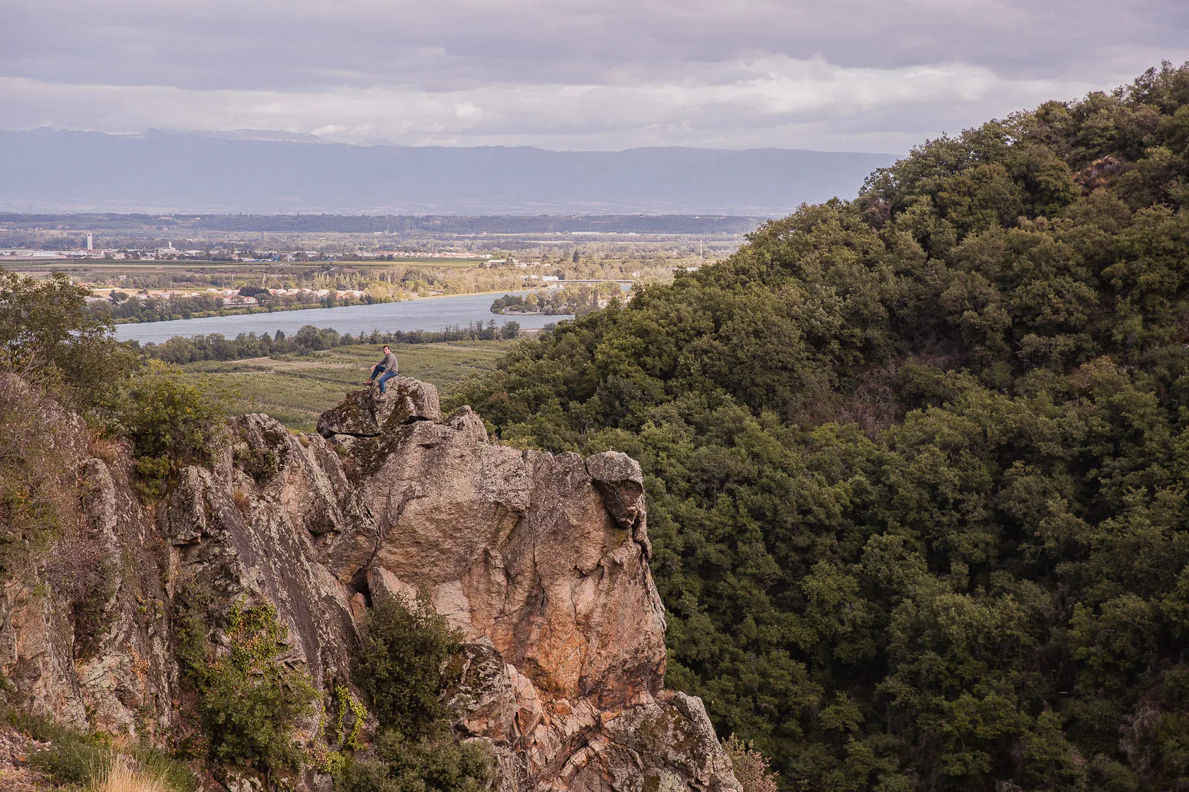 A rocky crag and wooded slopes above the river plain.