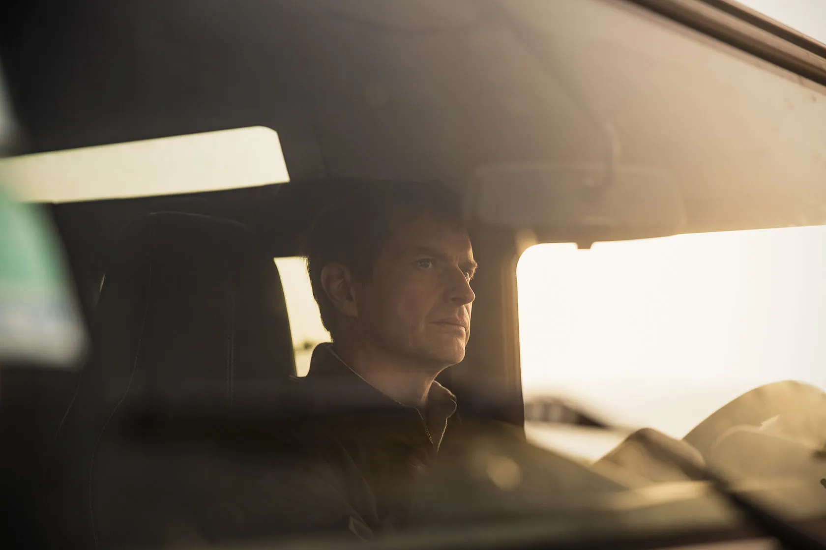 Jean-Louis Chave at the wheel of a car in warm evening light.