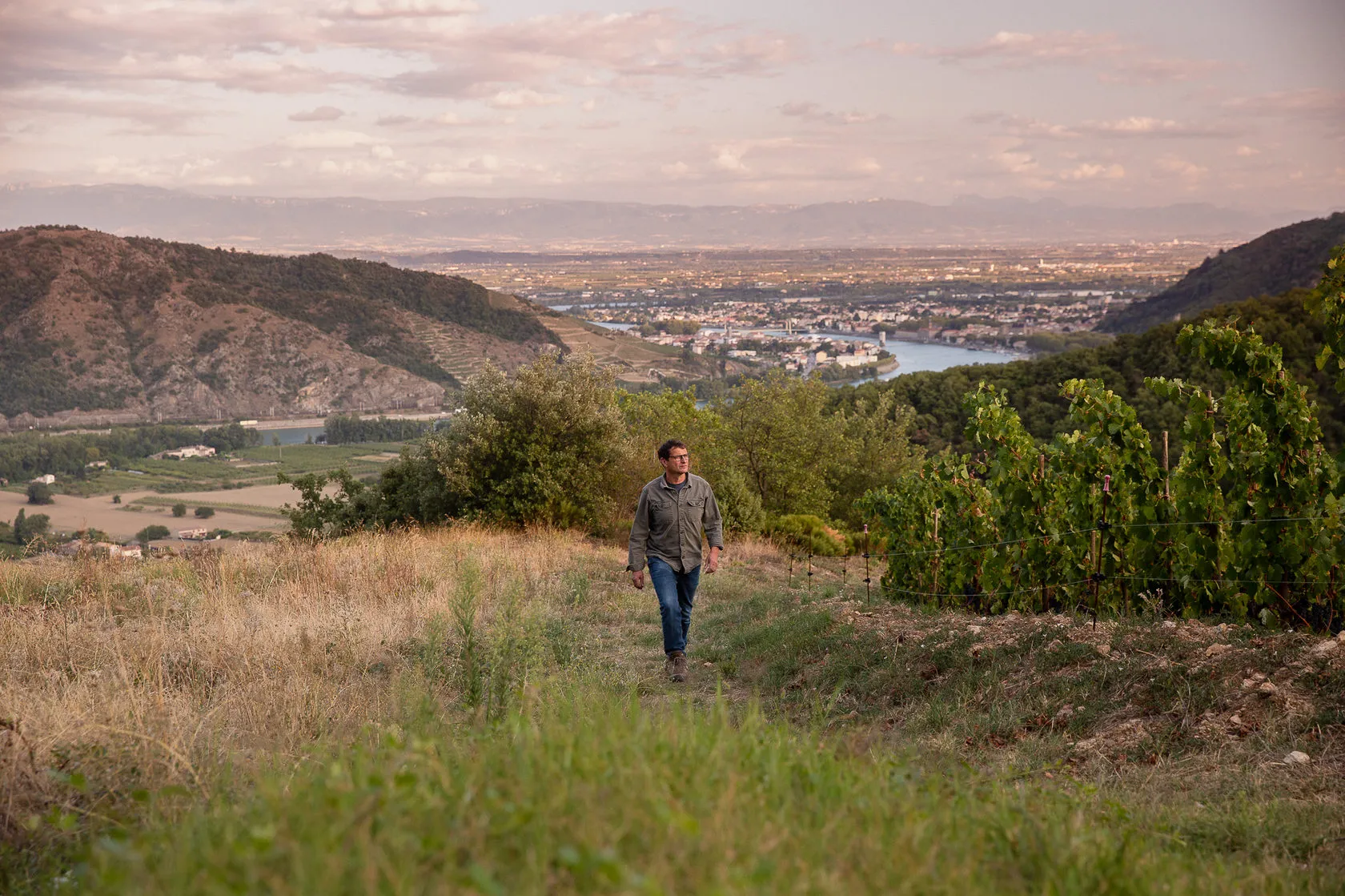 Jean-Louis Chave walks through tall grass on a hillside above the valley.