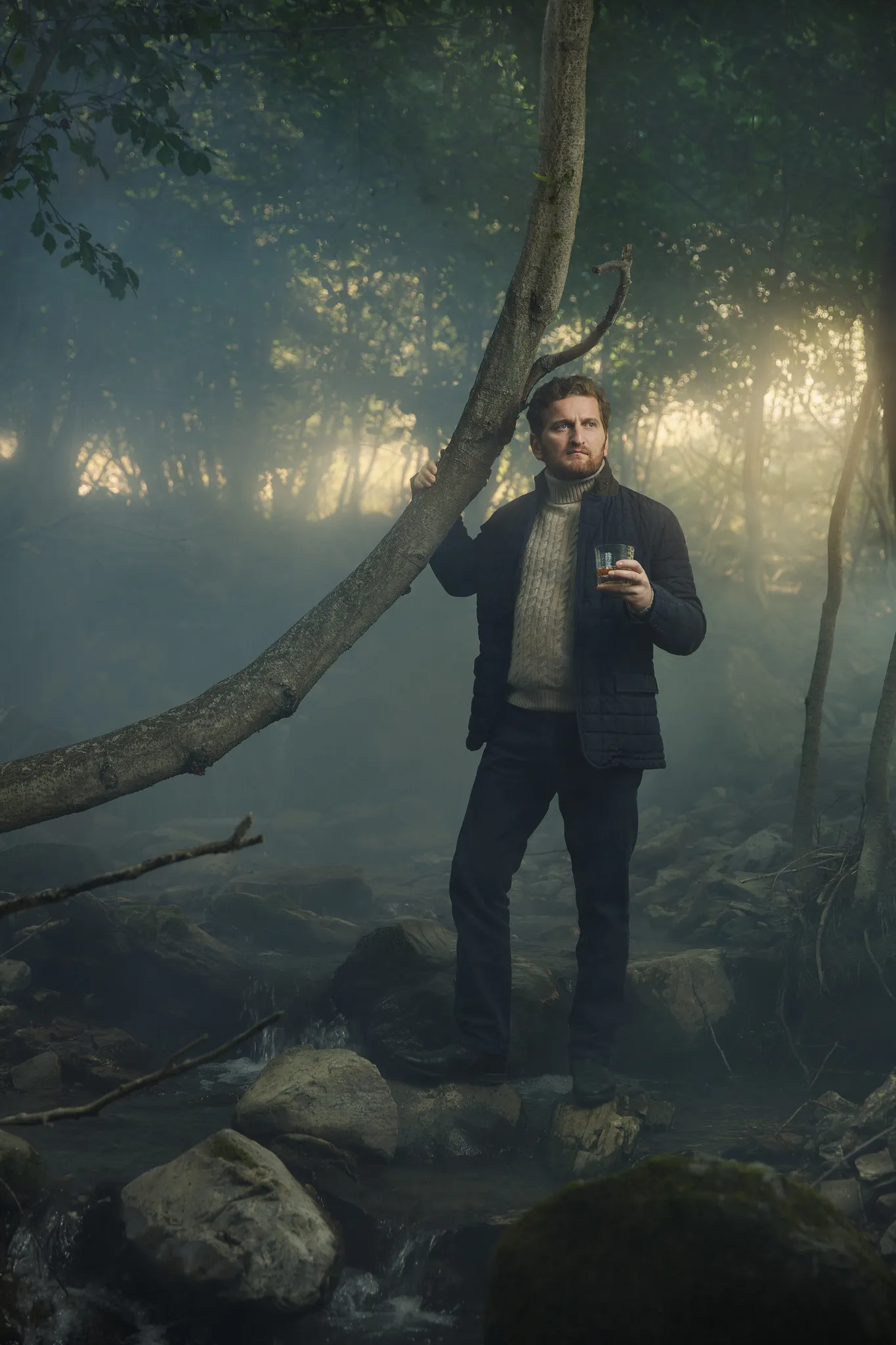Jimsher Chkhaidze stands in a misty forest, a glass in one hand, the other on a leaning branch.