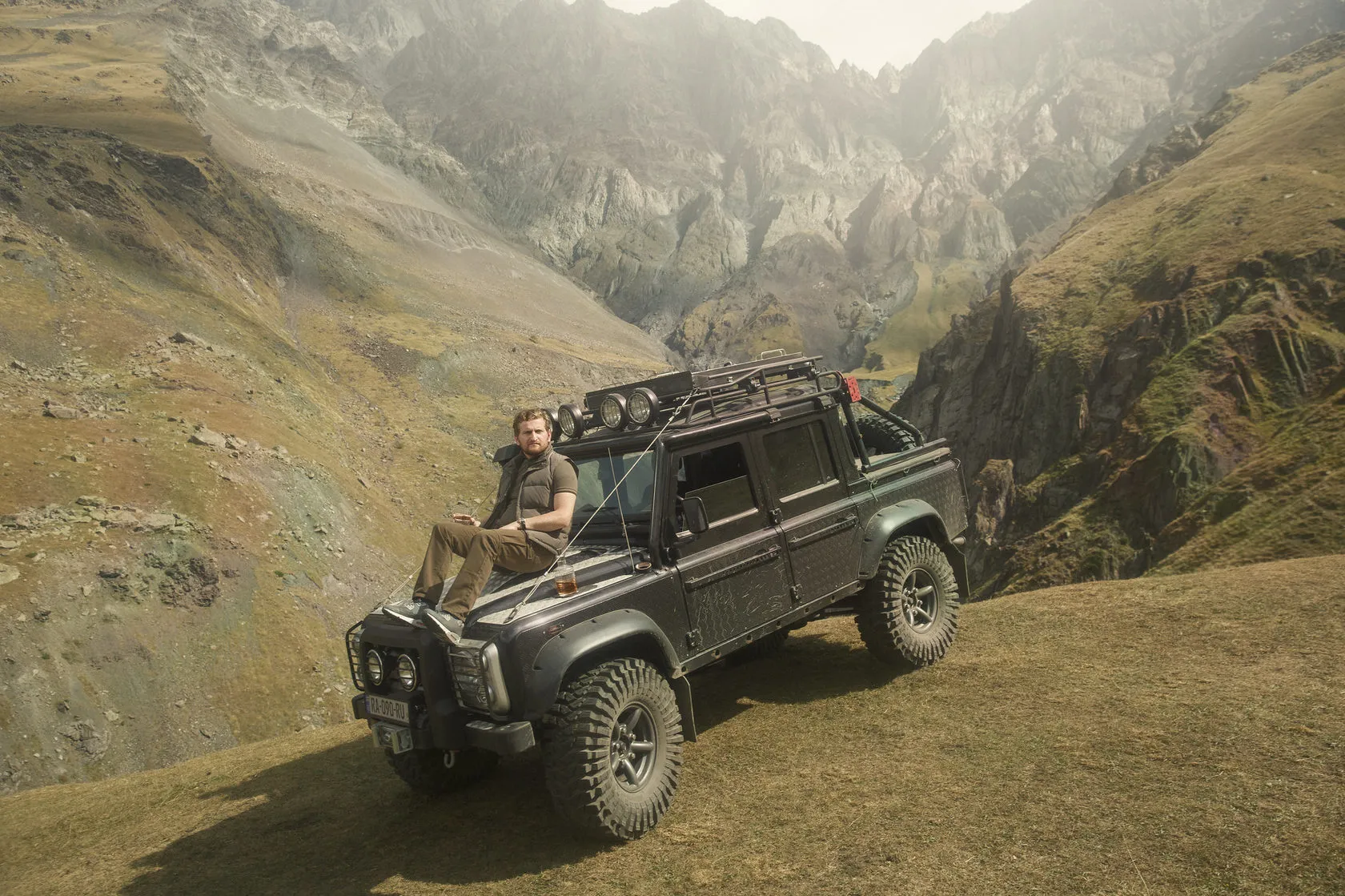 Jimsher Chkhaidze sits on the bonnet of an off-road truck in a mountain gorge.