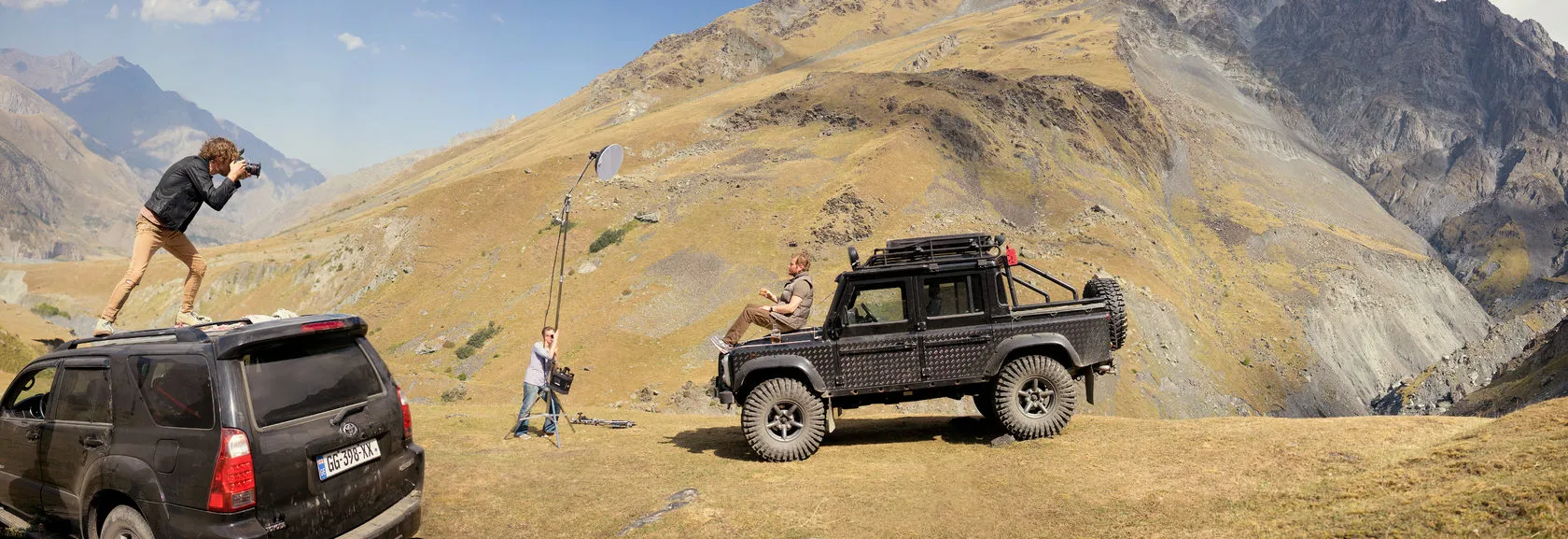 Behind the scenes: a photographer on a car roof shoots the truck on a mountain slope.