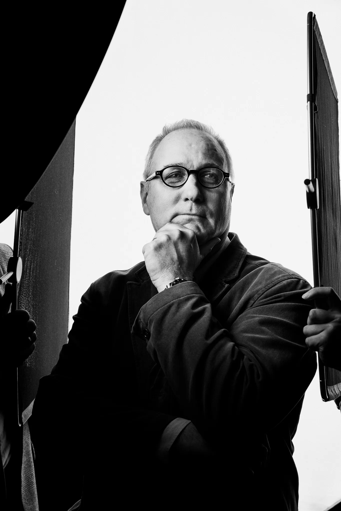 A Burgundy winemaker in round glasses, chin on his fist, framed by studio lights.