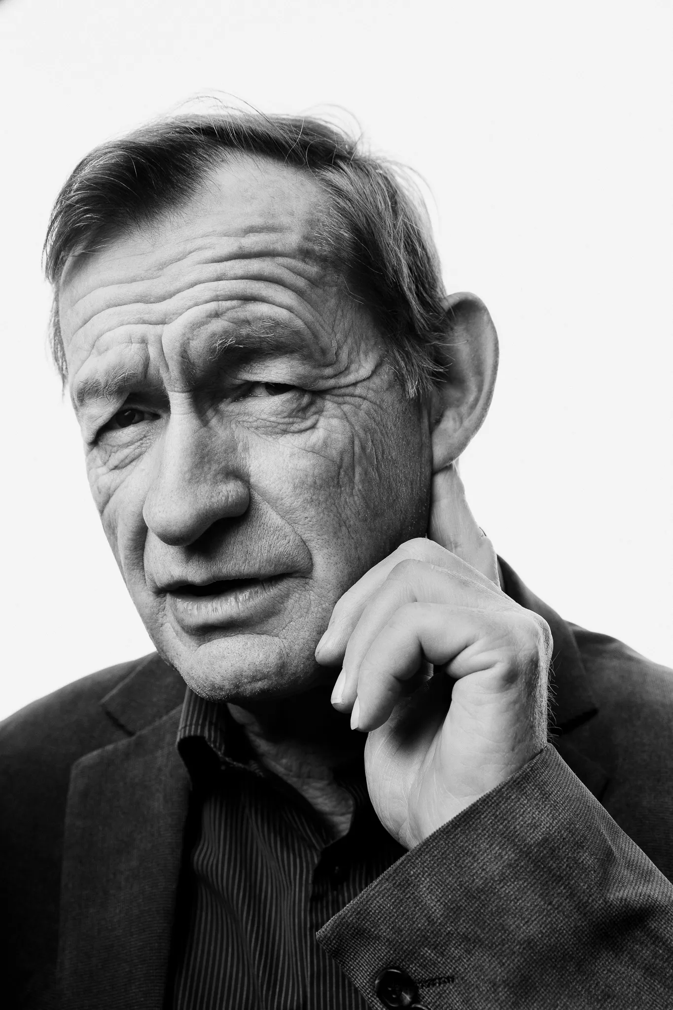 A grey-haired winemaker rests his cheek on his hand, in black and white.