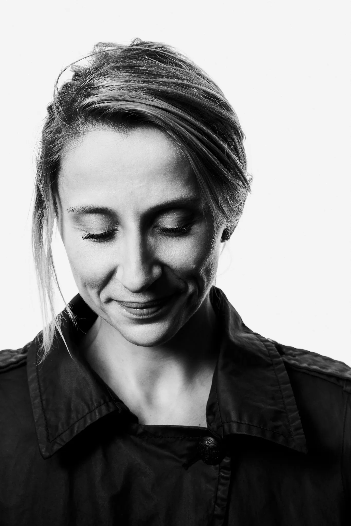 A young woman winemaker smiles and looks down, in black and white.