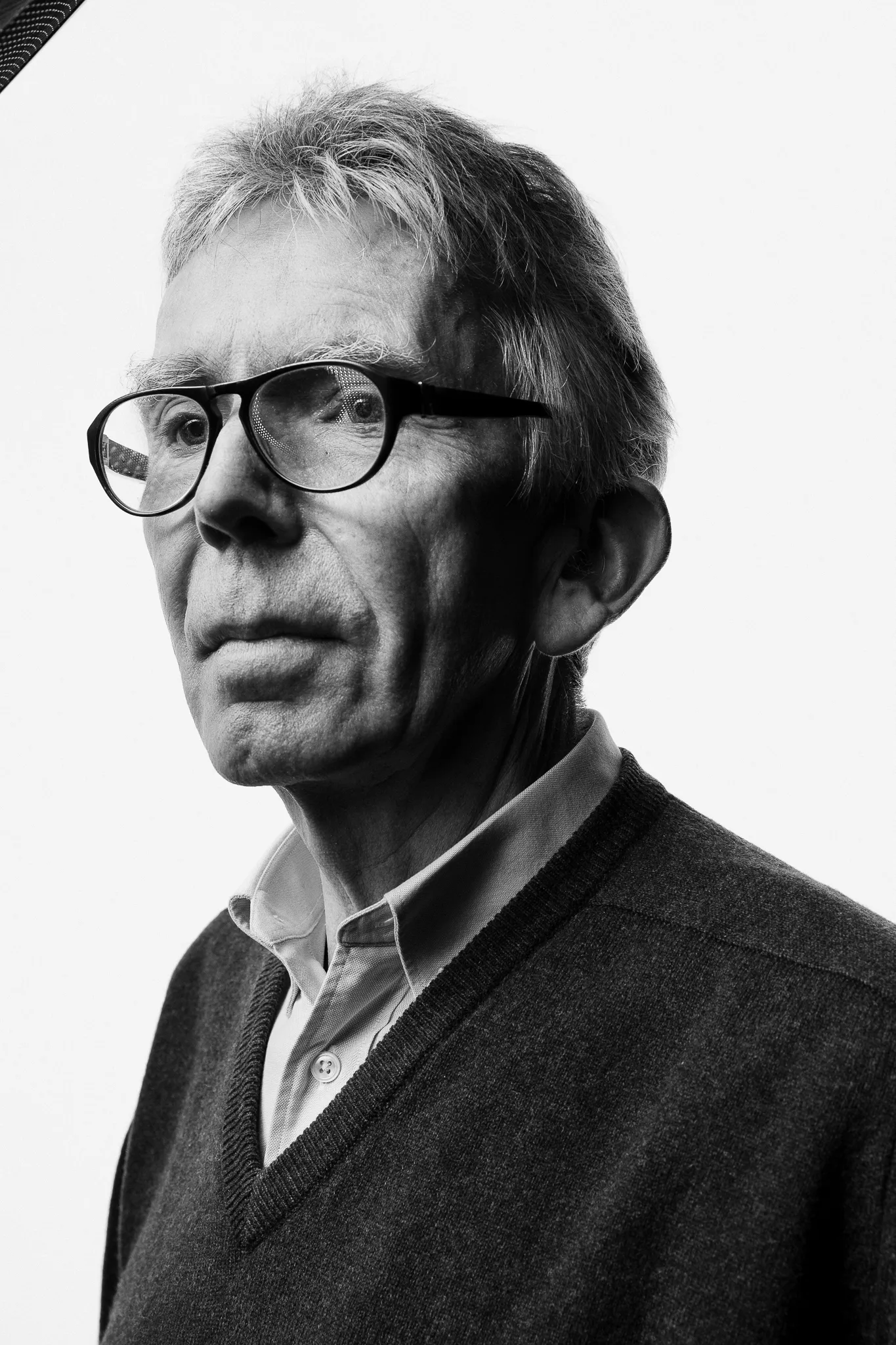 A winemaker in glasses and a V-neck jumper looks off to one side.