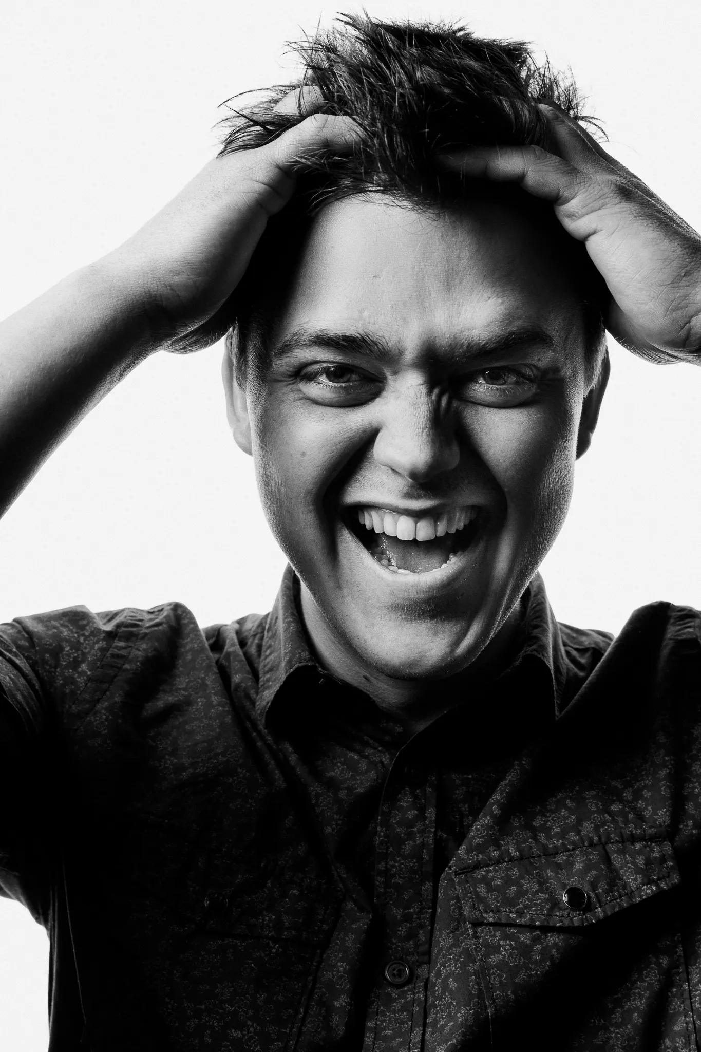 A young winemaker laughs, both hands in his hair.