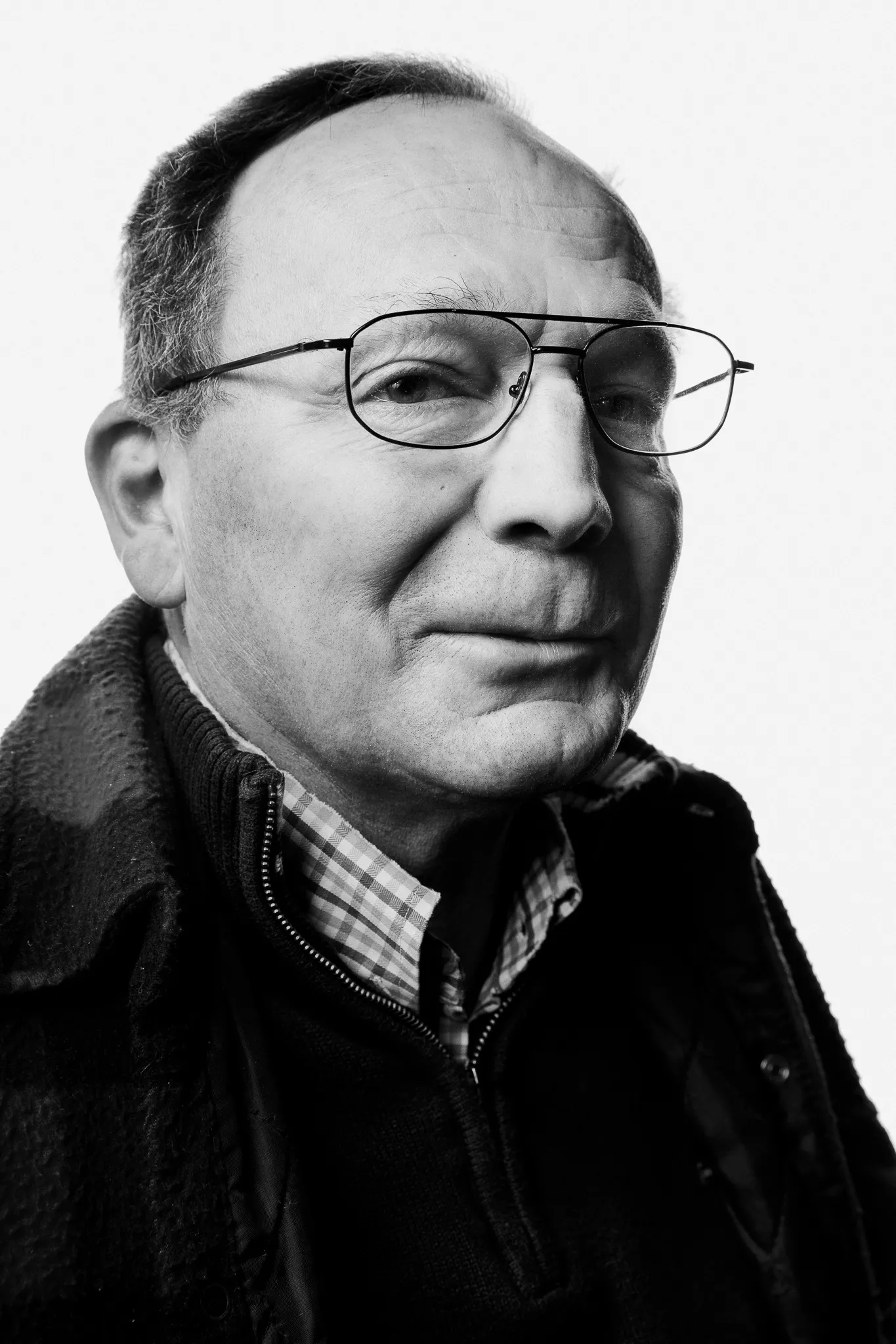 An older winemaker in wire glasses and a checked shirt half smiles.