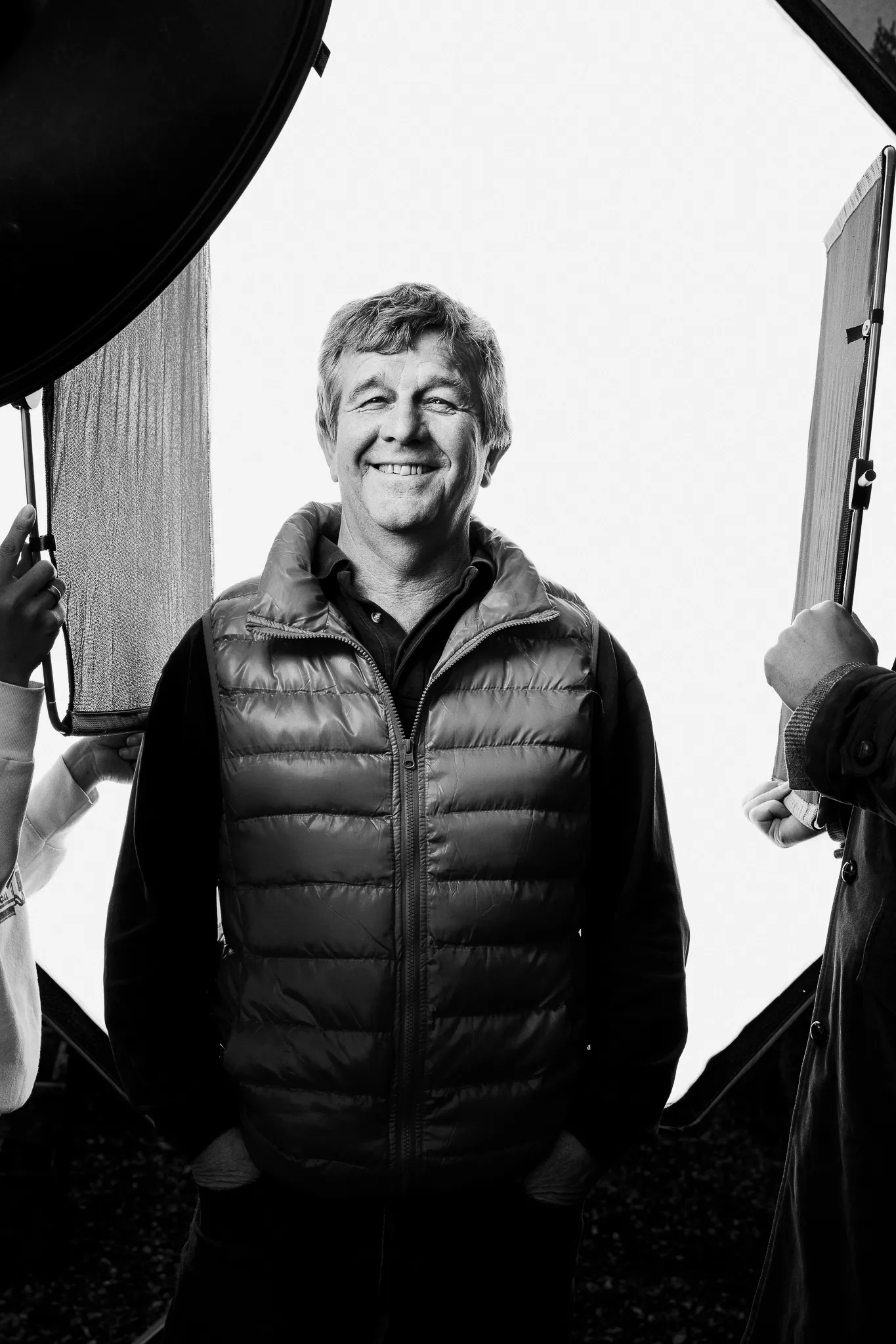A grinning winemaker in a puffer gilet stands between studio lights.