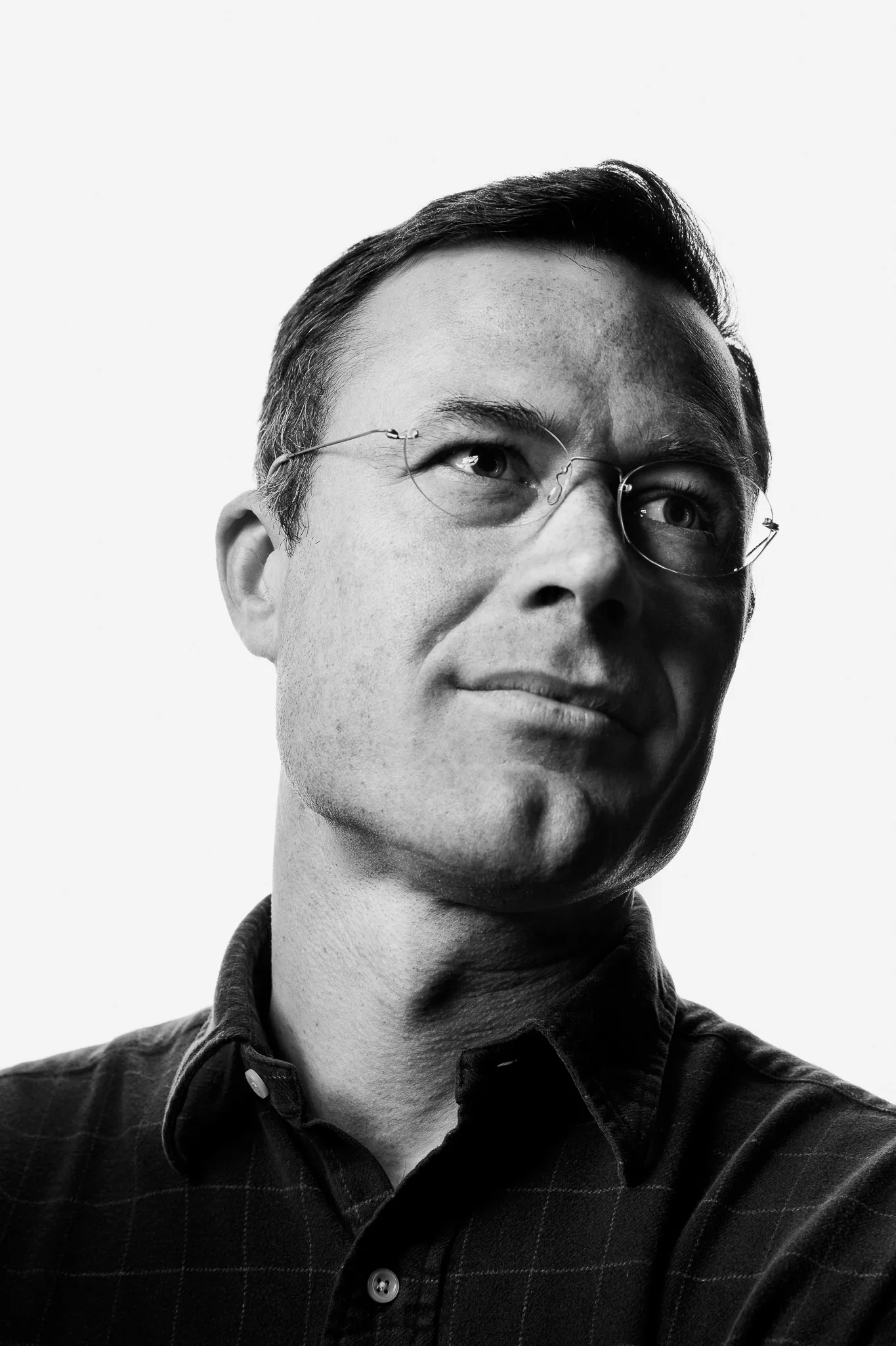 A winemaker in thin-rimmed glasses looks up and away.