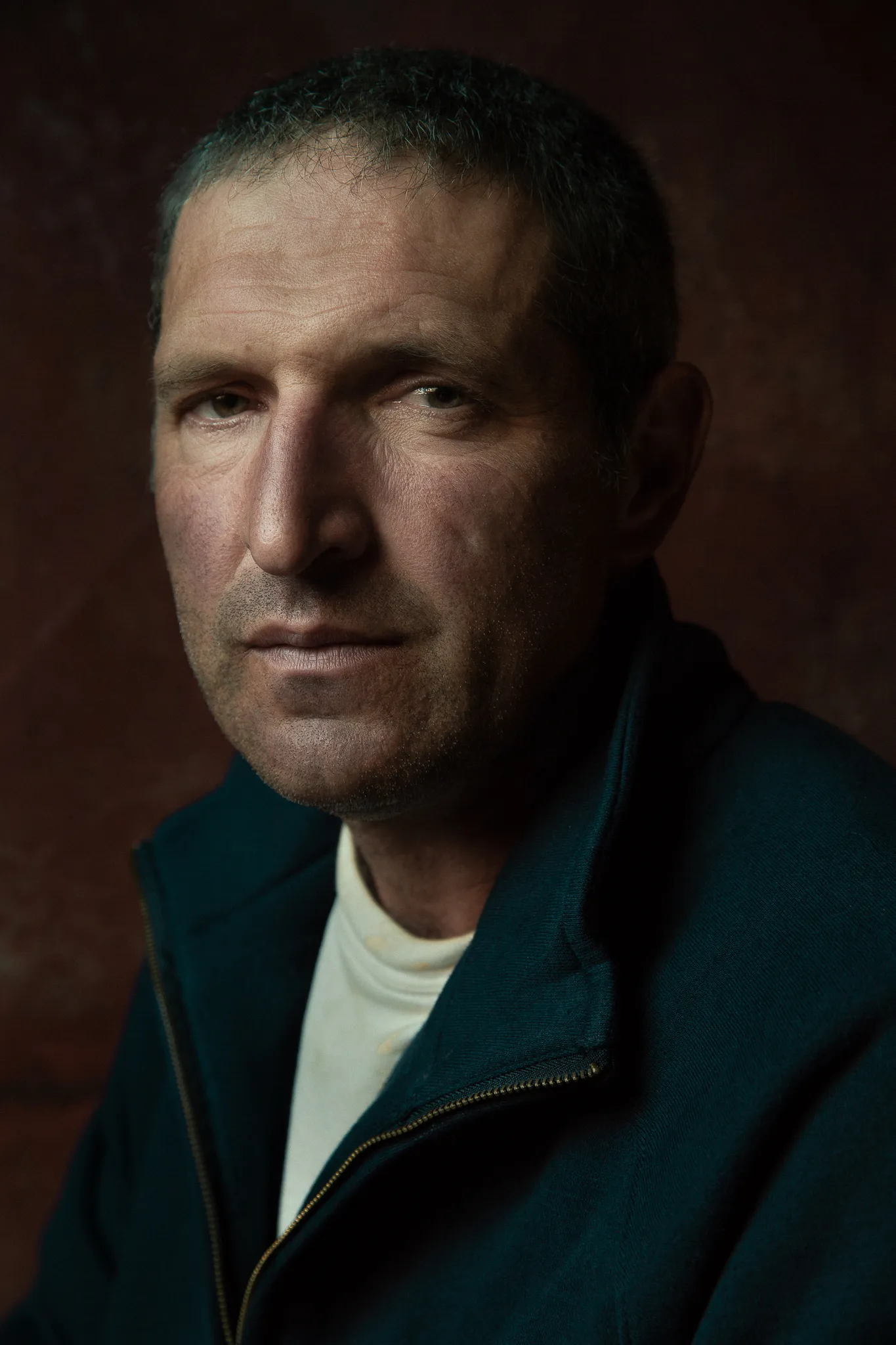 Jean-Claude Ramonet in a dark zip jacket, close up against a rust-brown wall.