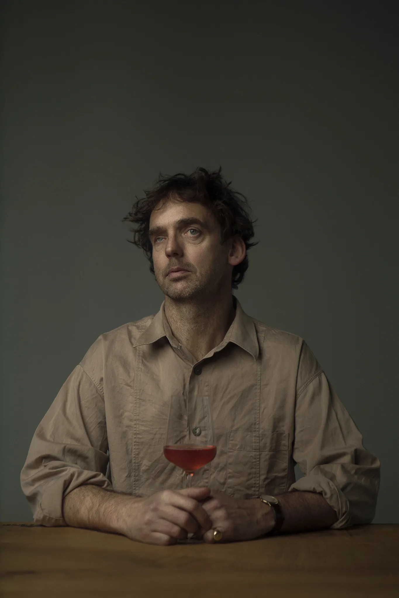 Sean O’Callaghan sits at a table with a glass of pale red wine, looking up.