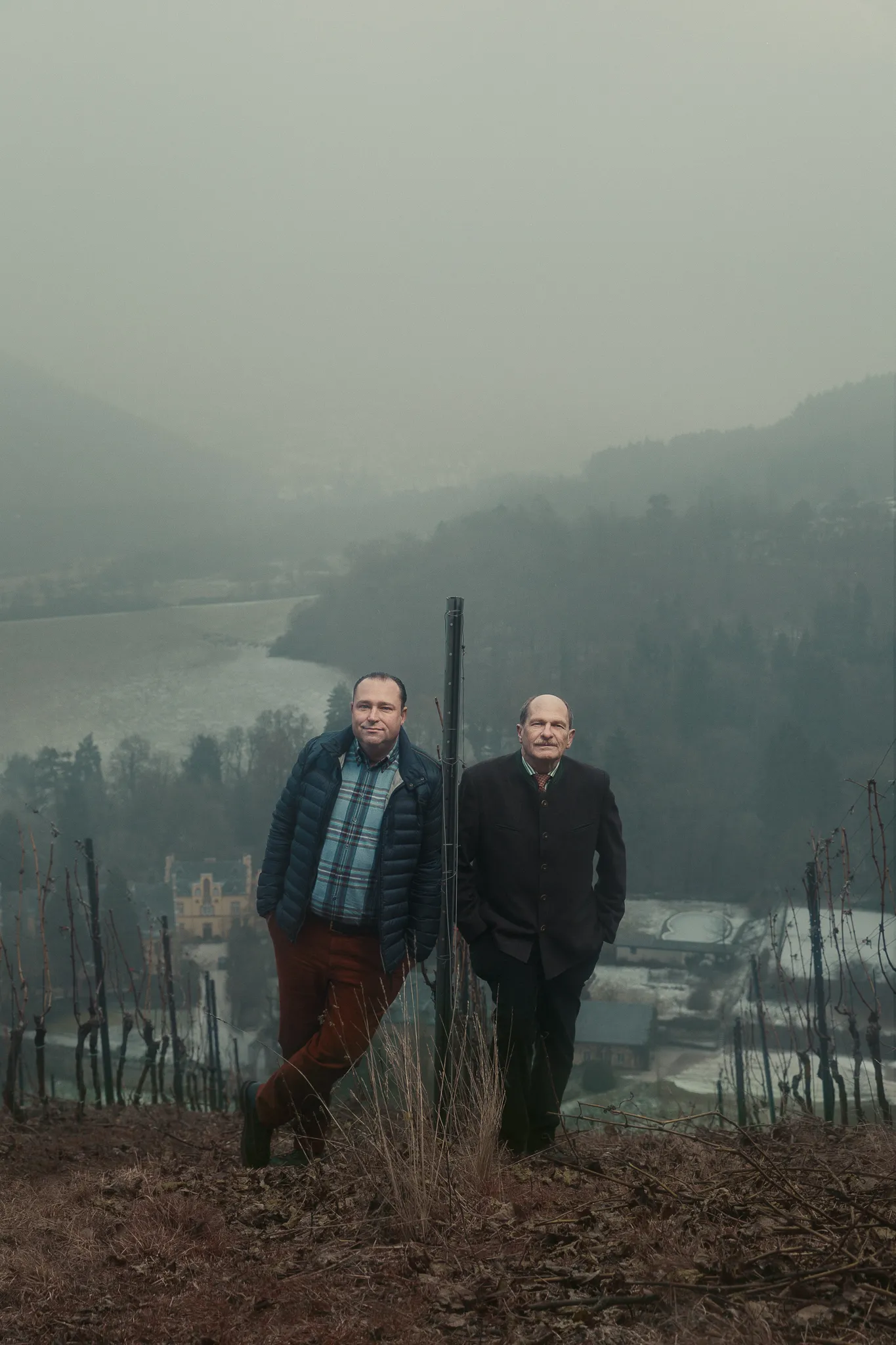 Nik Weis and Carl von Schubert stand in a misty vineyard above a river valley.