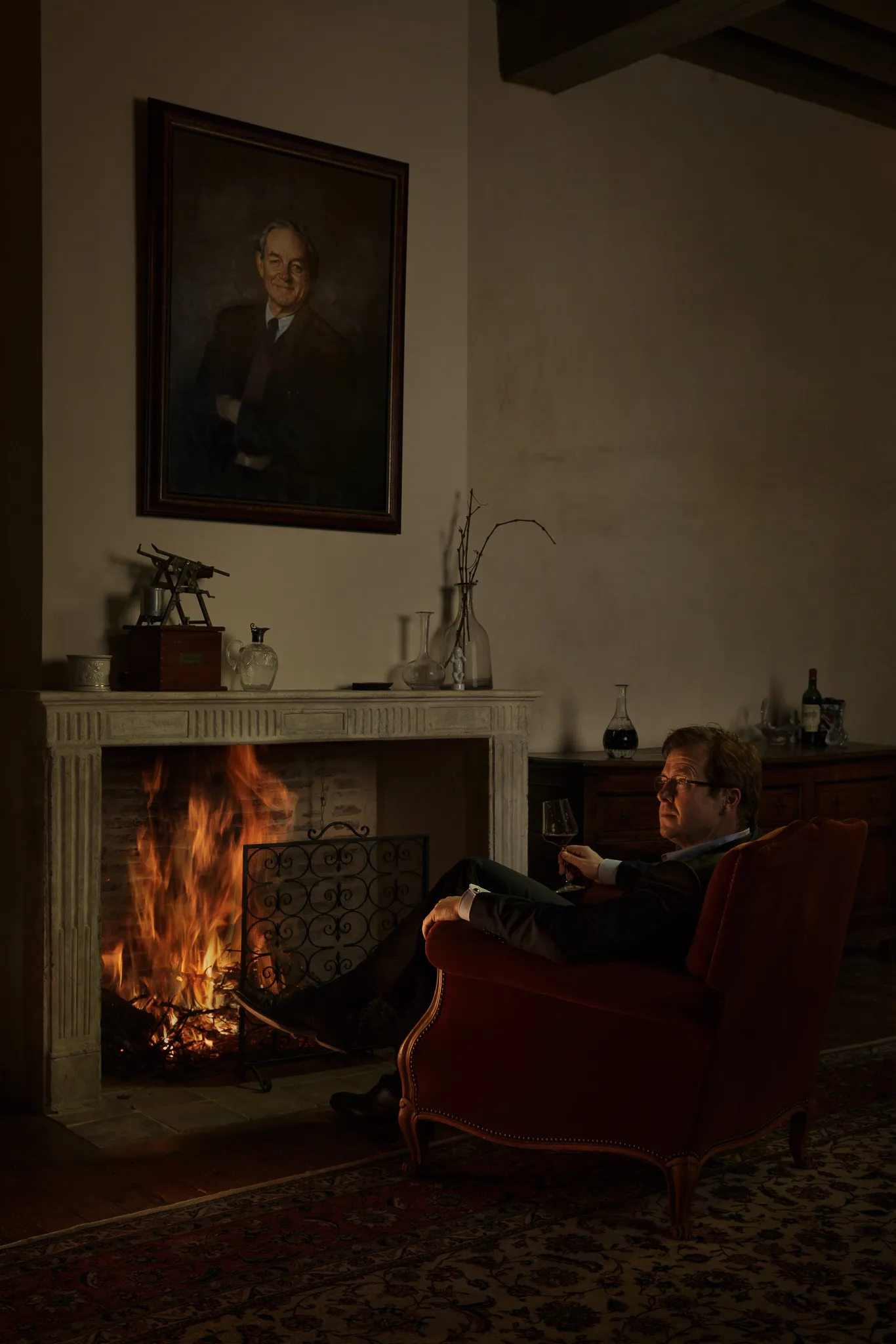David Sichel sits by a lit fireplace beneath a painted portrait.