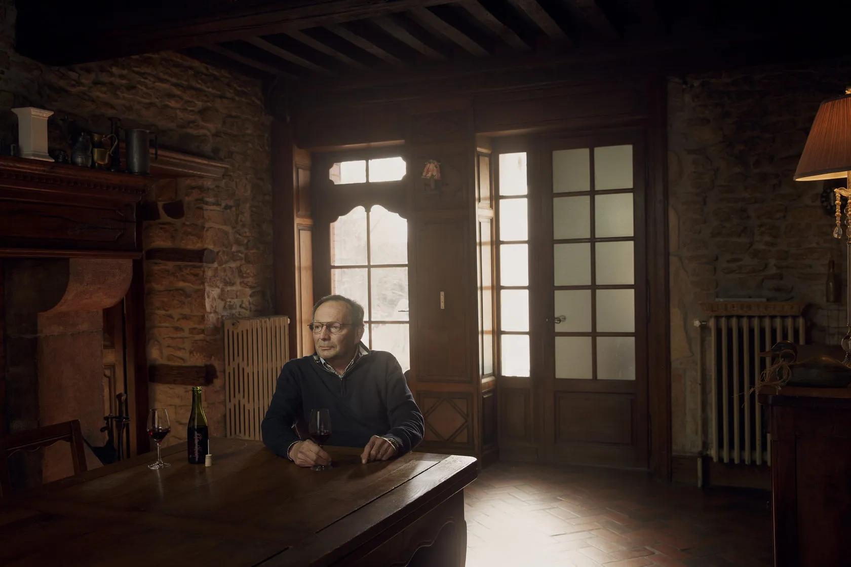 Bruno Clair sits at a wooden table in a stone-walled room by tall windows.