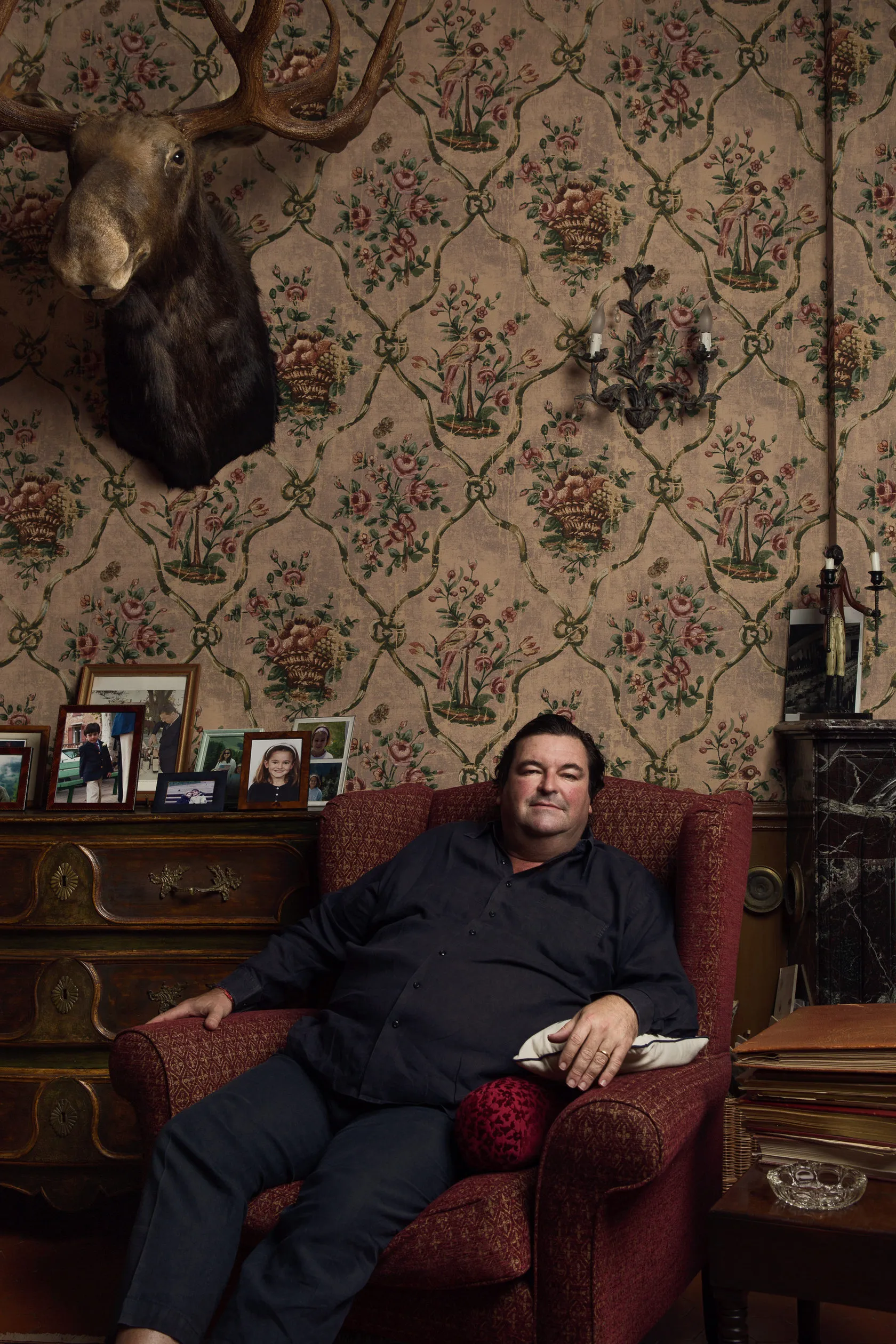Sacha Alexis Lichine lounges in a red armchair beneath a mounted moose head.