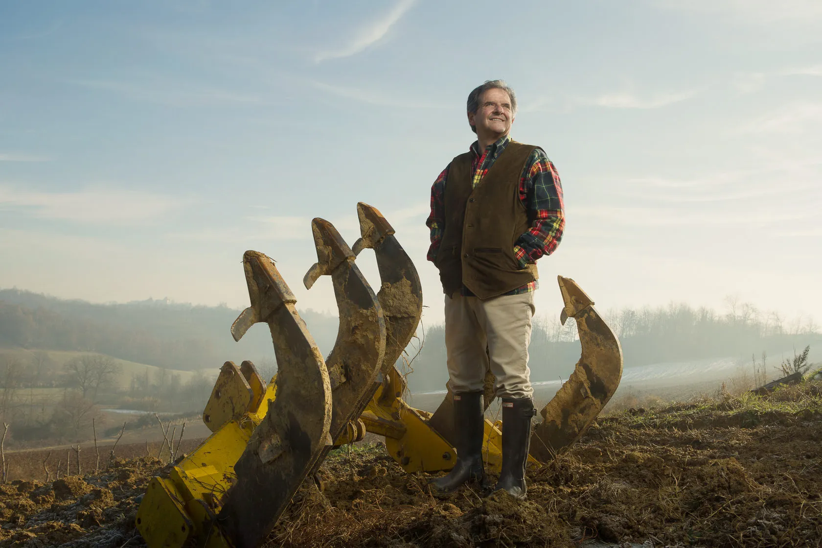 Dr Donato Lanati stands on a ploughed field beside giant yellow plough tines.