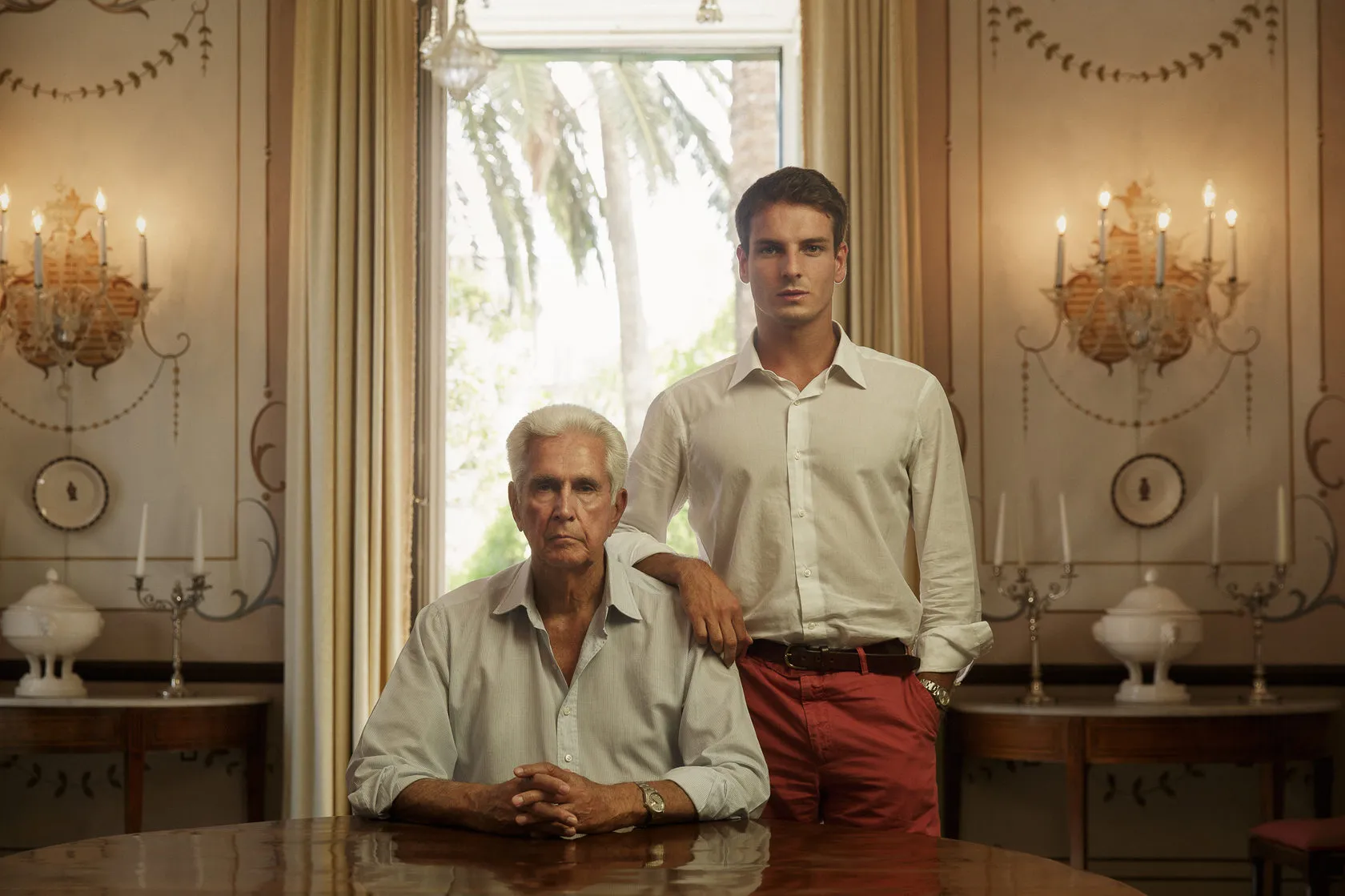 Alcibiade Zecca sits at a table in a grand room, his nephew standing beside him.