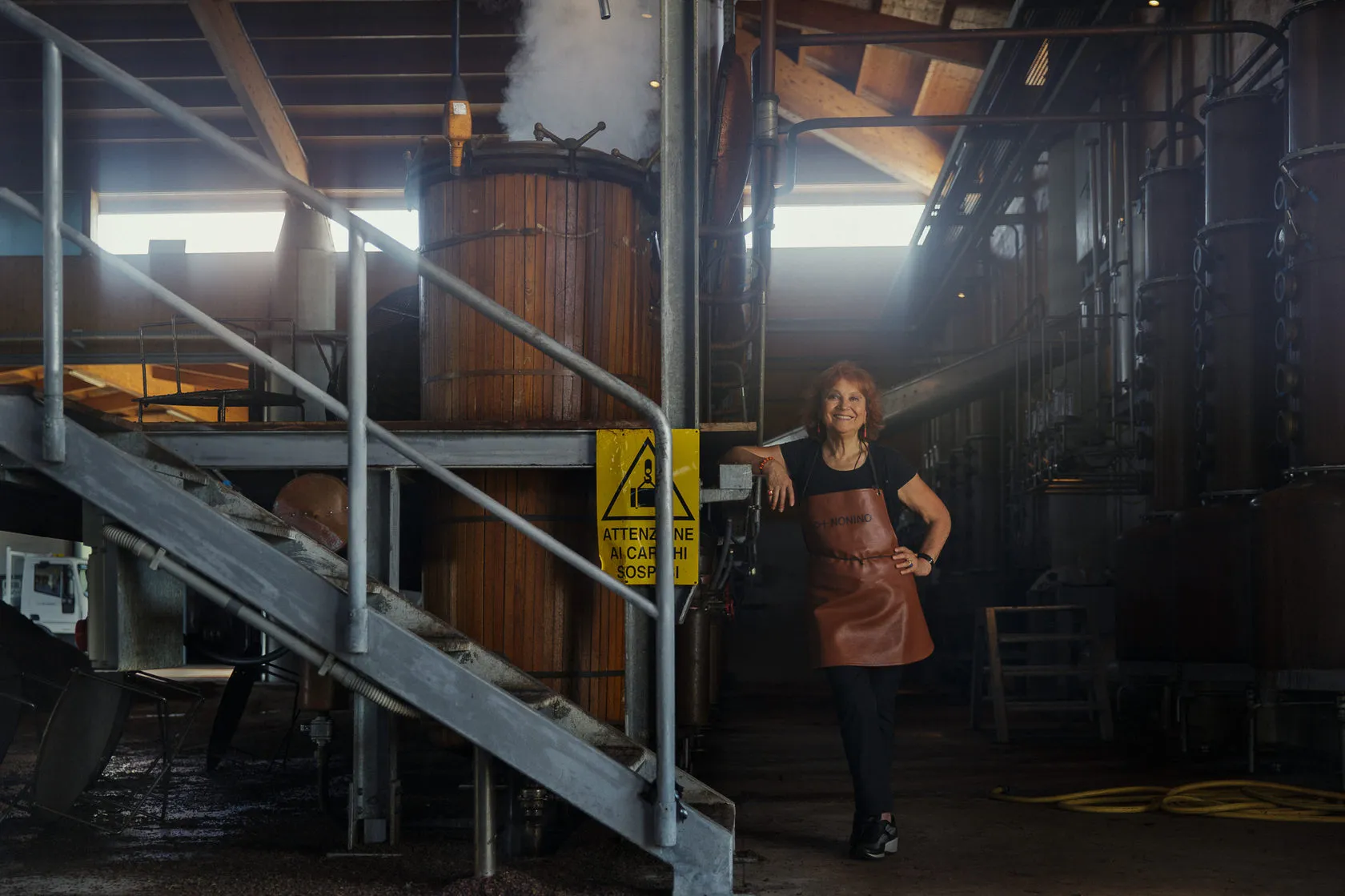 A woman in a leather apron stands by a steel staircase in the Nonino distillery.