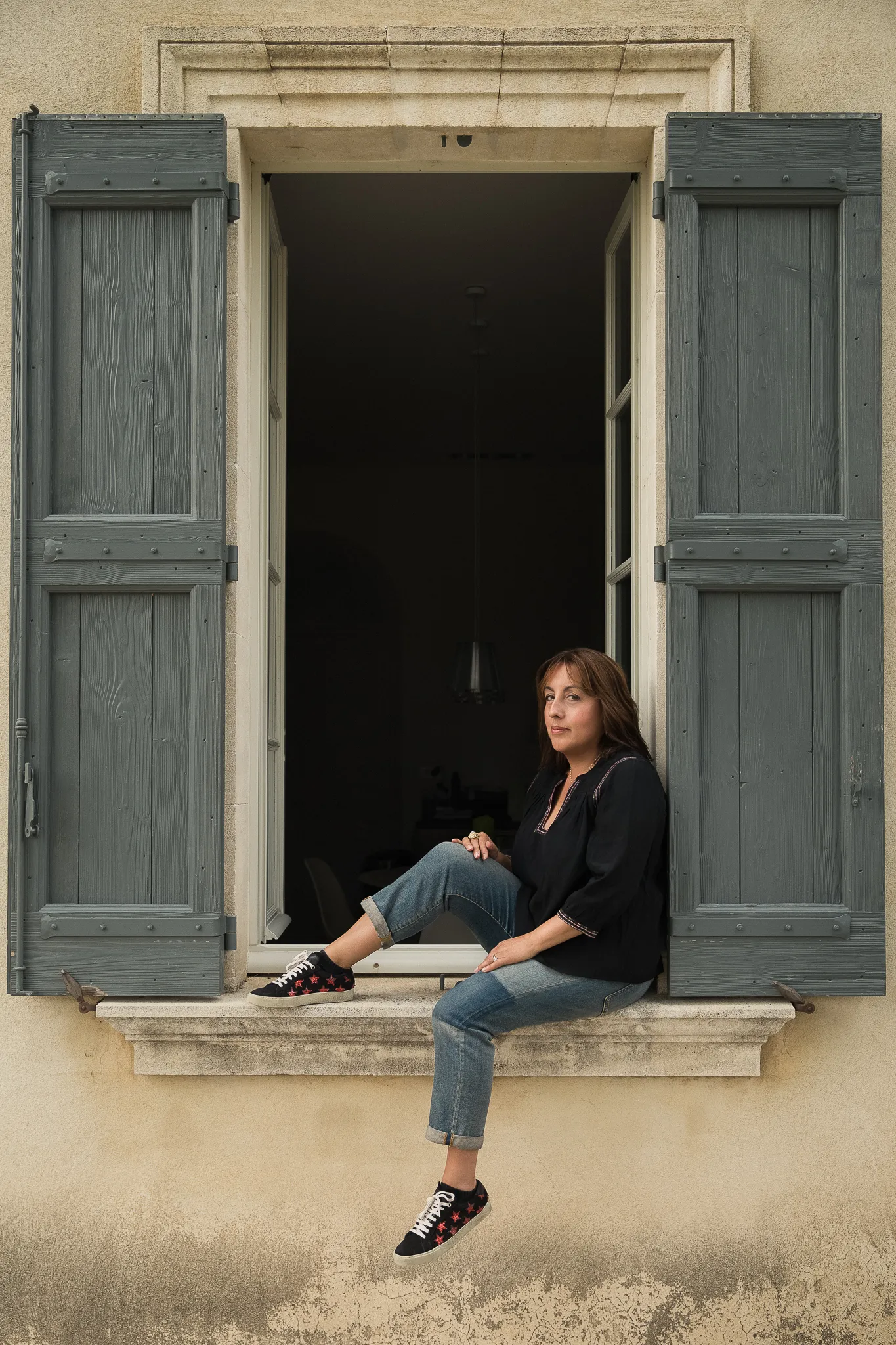 A winemaker sits on a windowsill between grey-green shutters.
