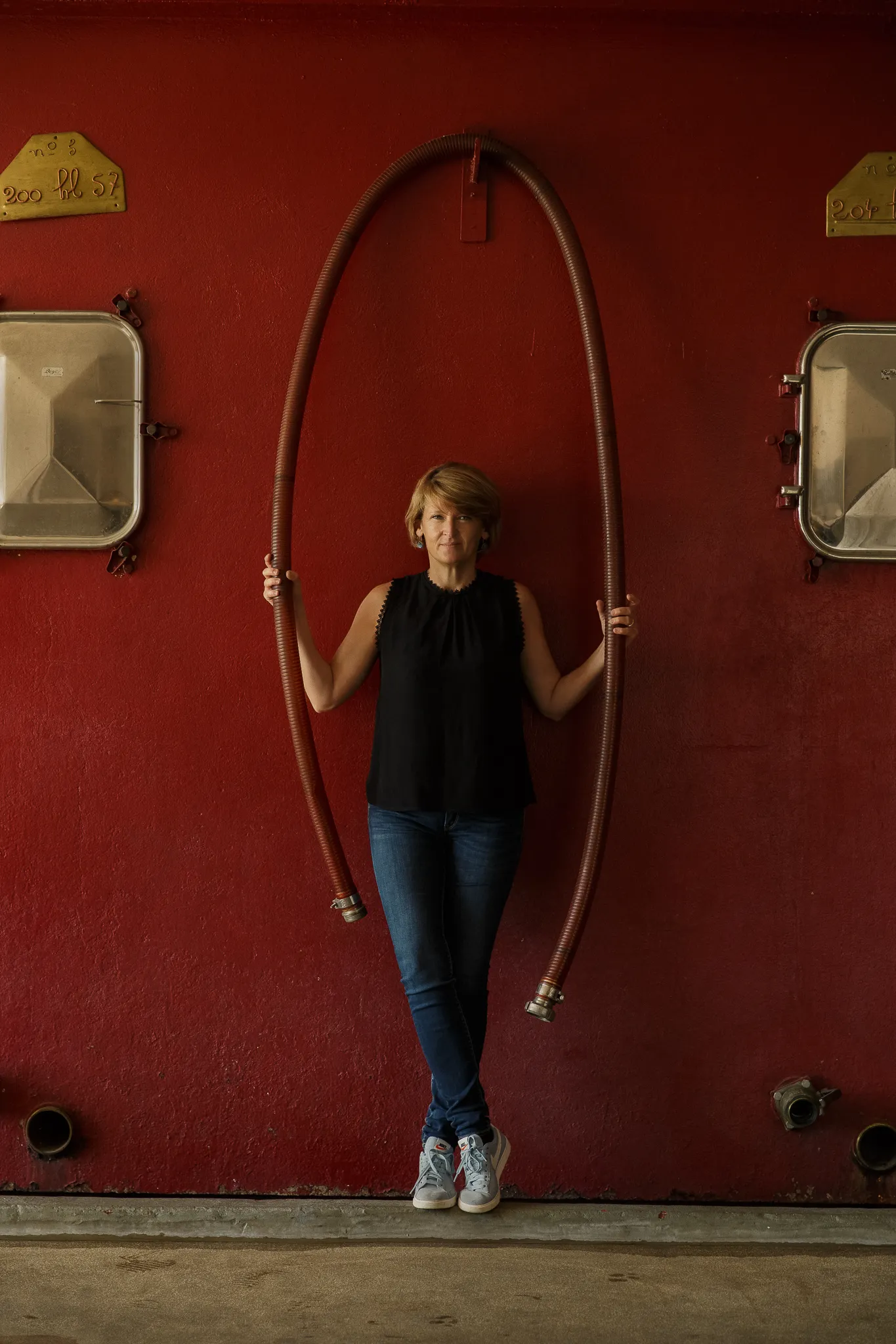 A winemaker stands under a loop of hose against a red vat.
