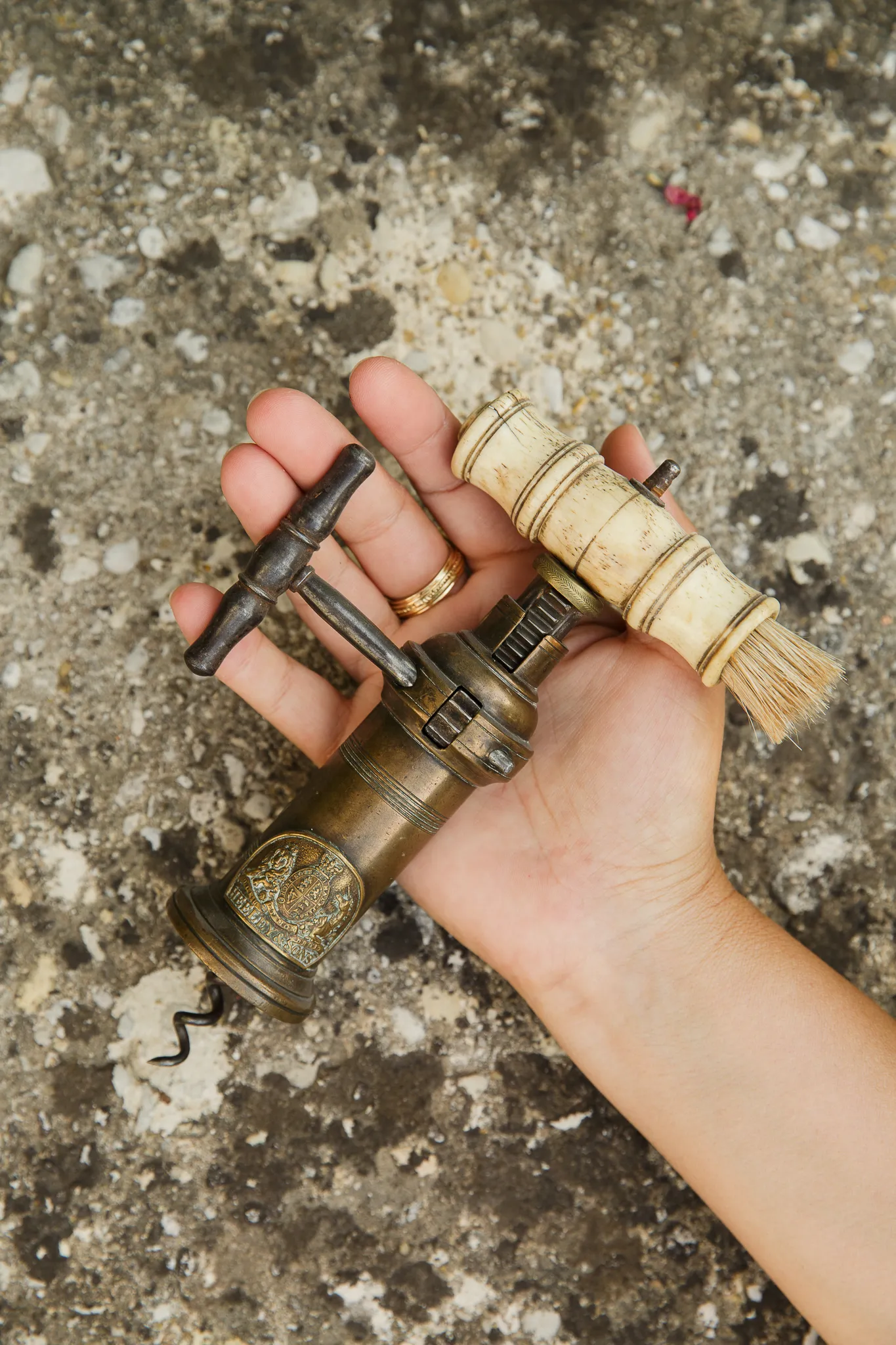 A hand holds an antique corkscrew with a brush handle.